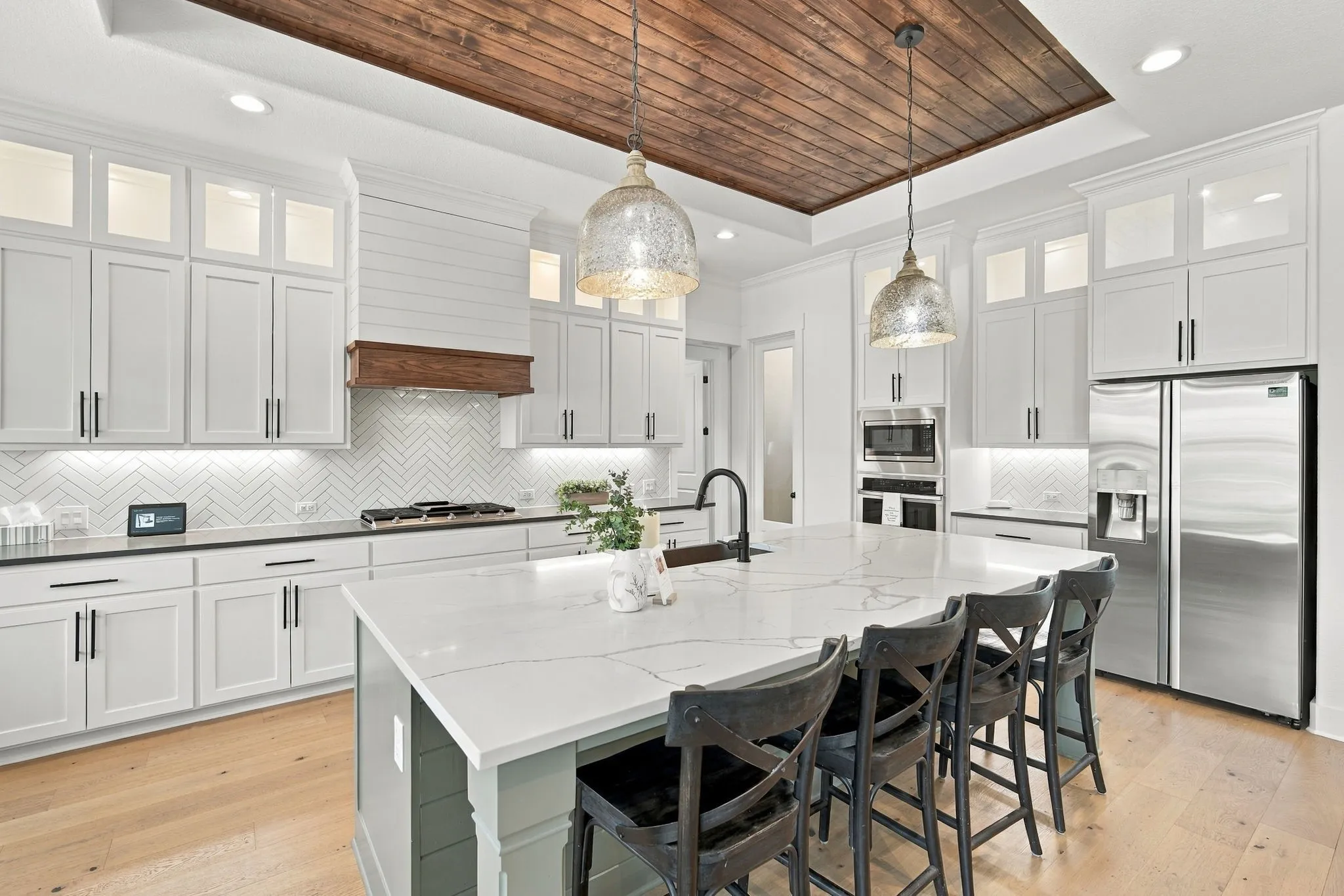White shaker cabinetry with black hardware, quartz countertop, stainless steel appliances, and a tongue and groove insert in the Tres ceiling.