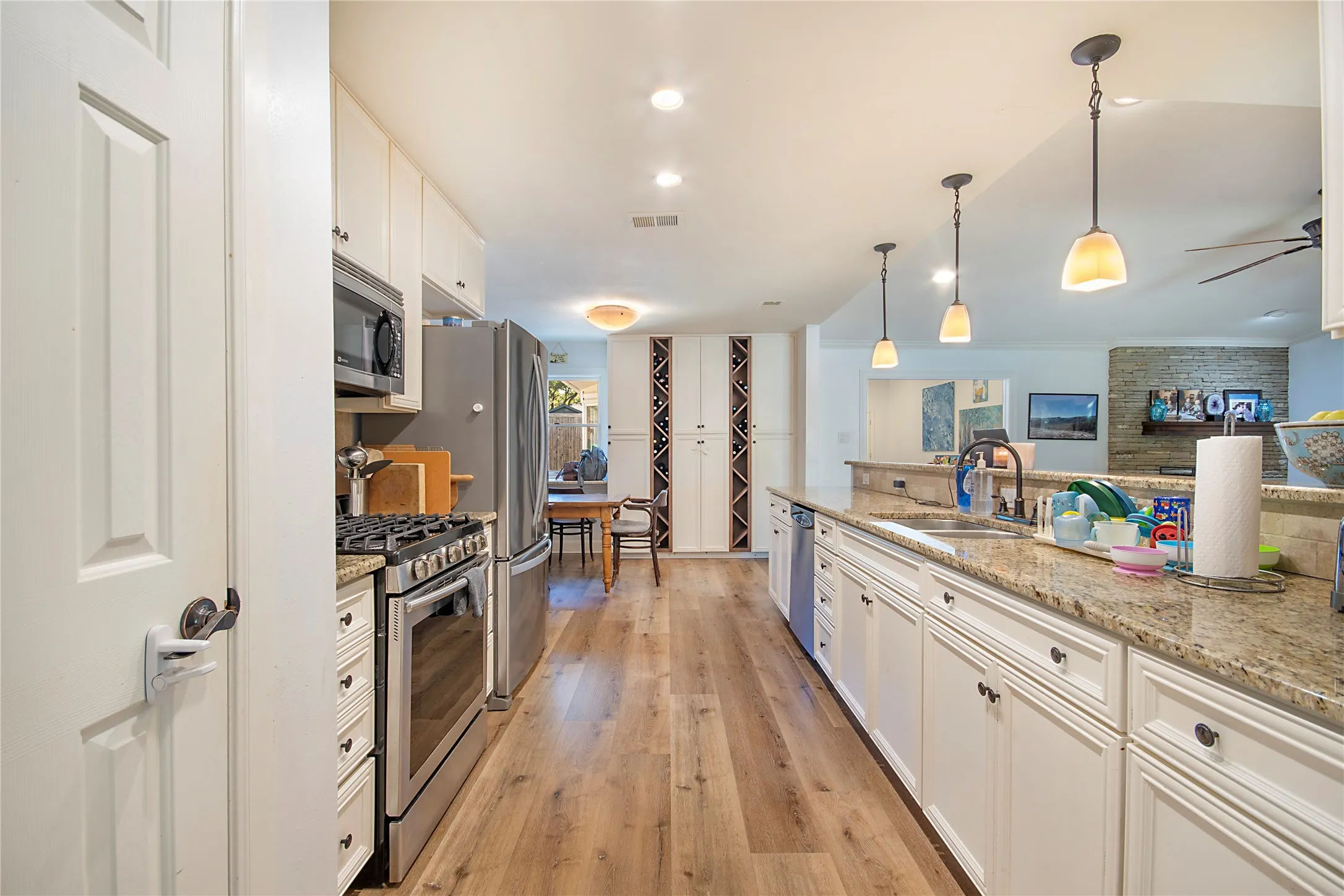 Galley kitchen with wood-finish flooring, white cabinetry, granite countertops, and stainless-steel appliances