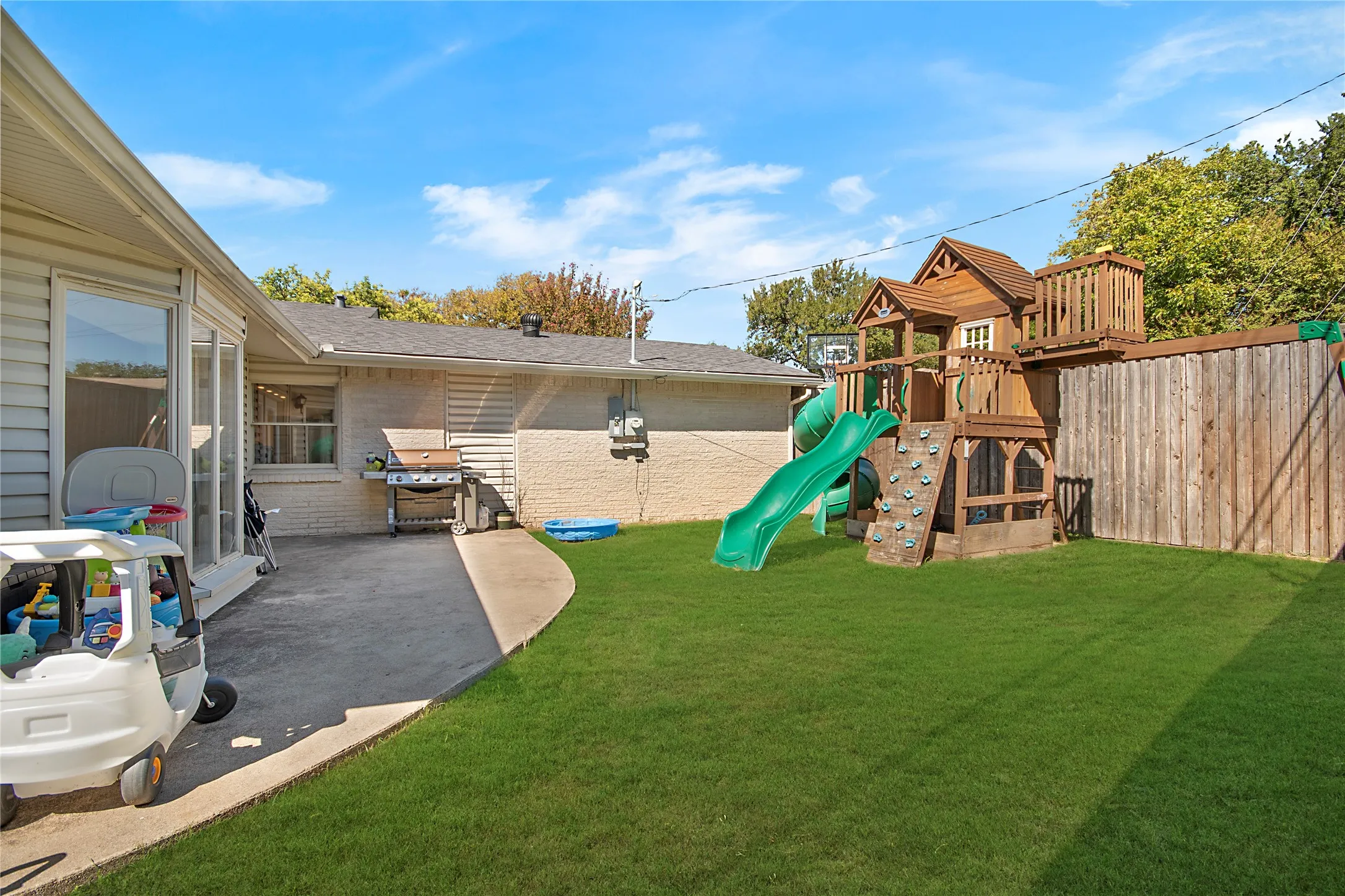 Expansive backyard featuring a manicured lawn, concrete patio, and a wood privacy fence