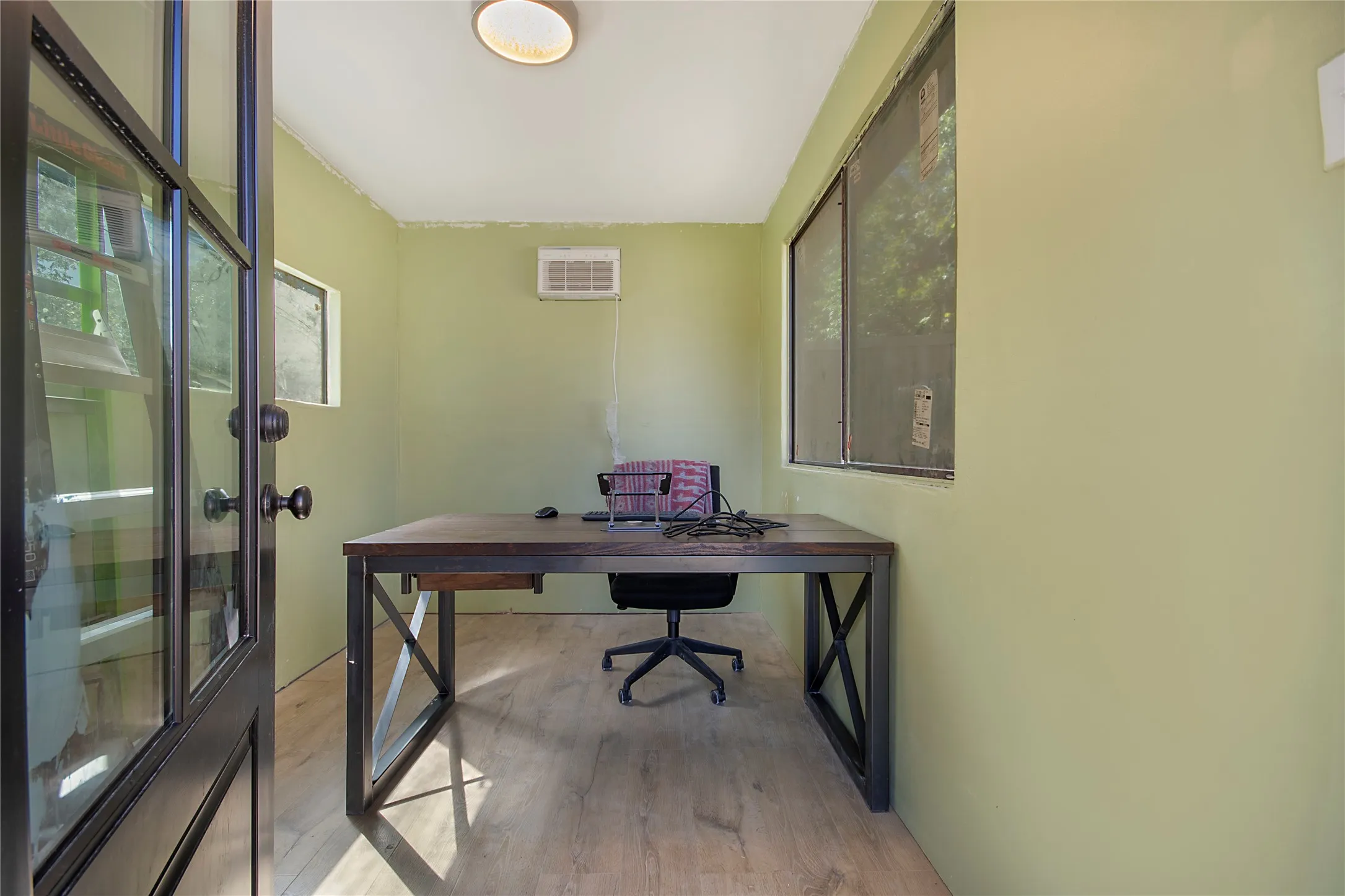 Dedicated home office featuring a sturdy wood-finish desk with X-frame styling, wood-finish flooring, and abundant natural light from dual glass doors and windows