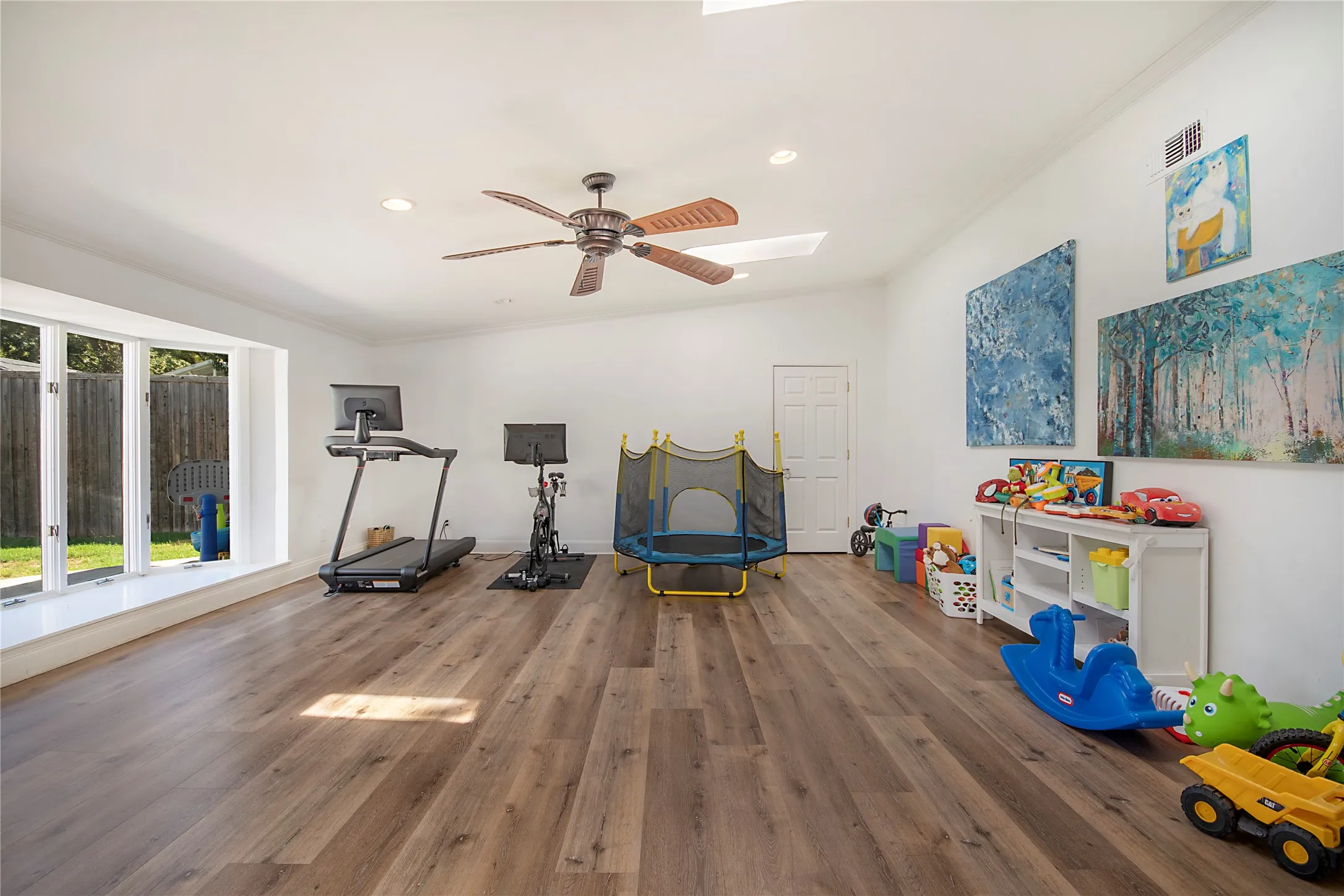 Spacious room with wood-finish flooring, a large bay window, and a ceiling fan
