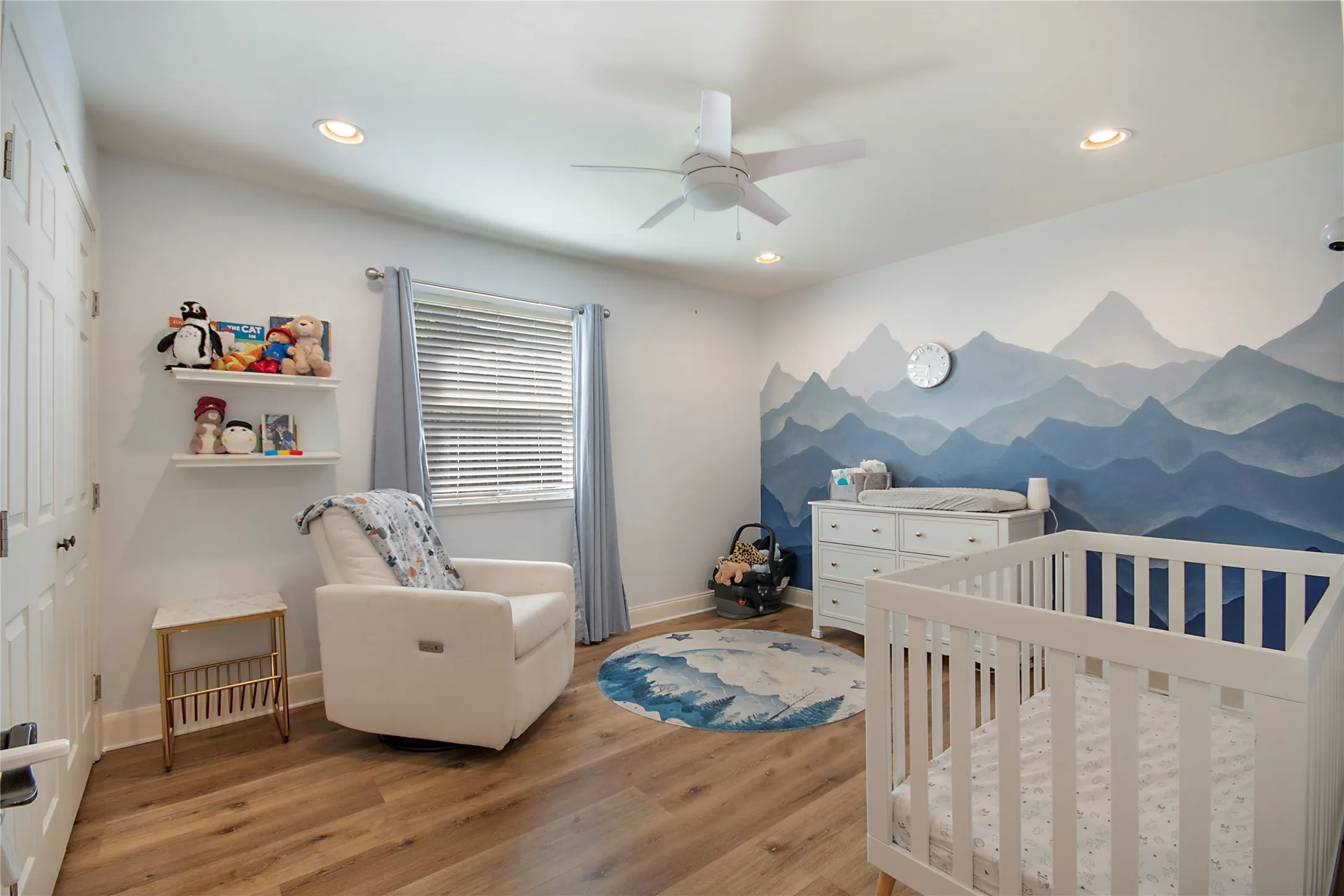 Wood-finish flooring with a white dresser, crib, and a wall mural