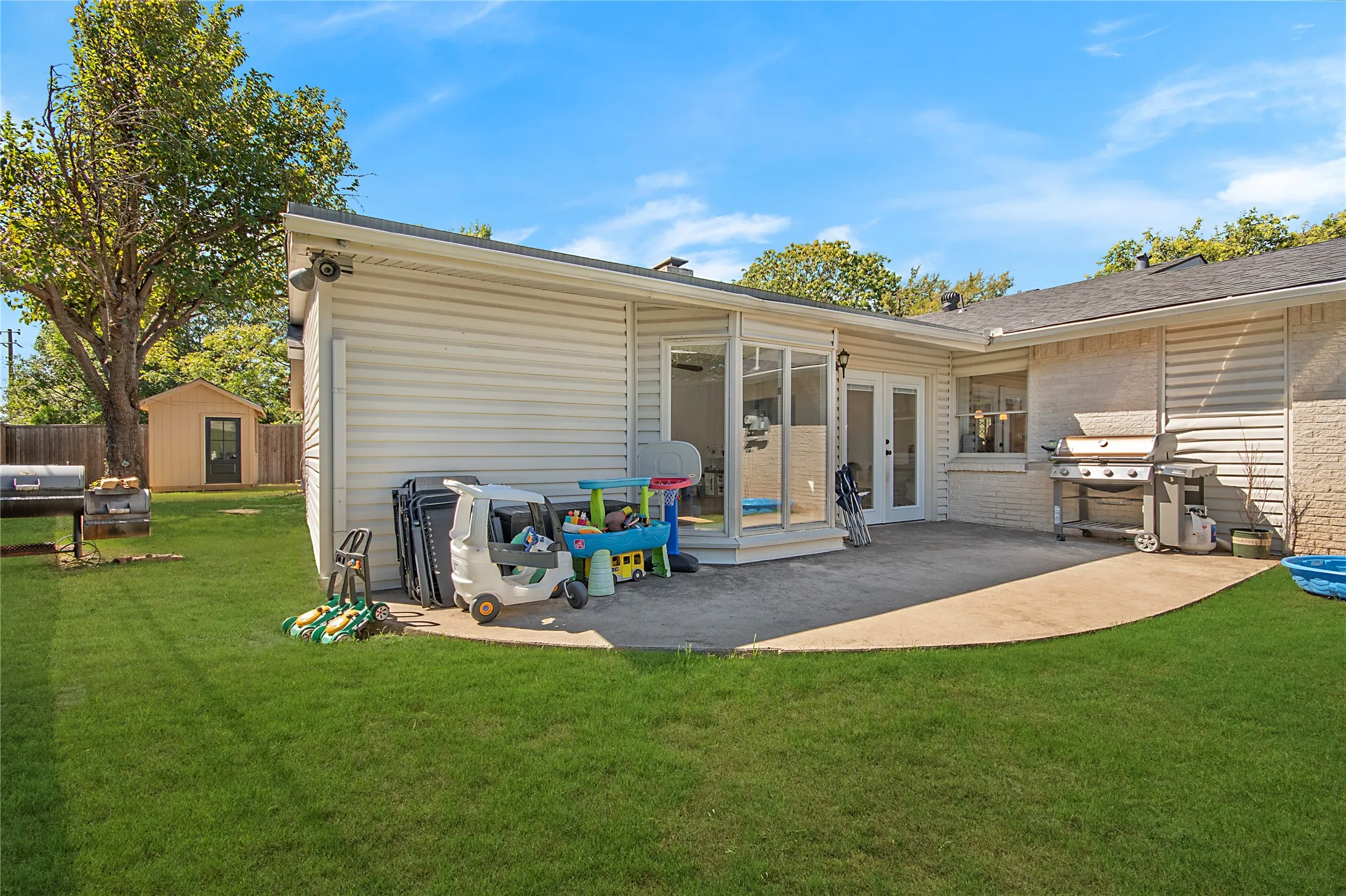 Expansive backyard with a manicured lawn, concrete patio, and a sunroom featuring full-light double doors