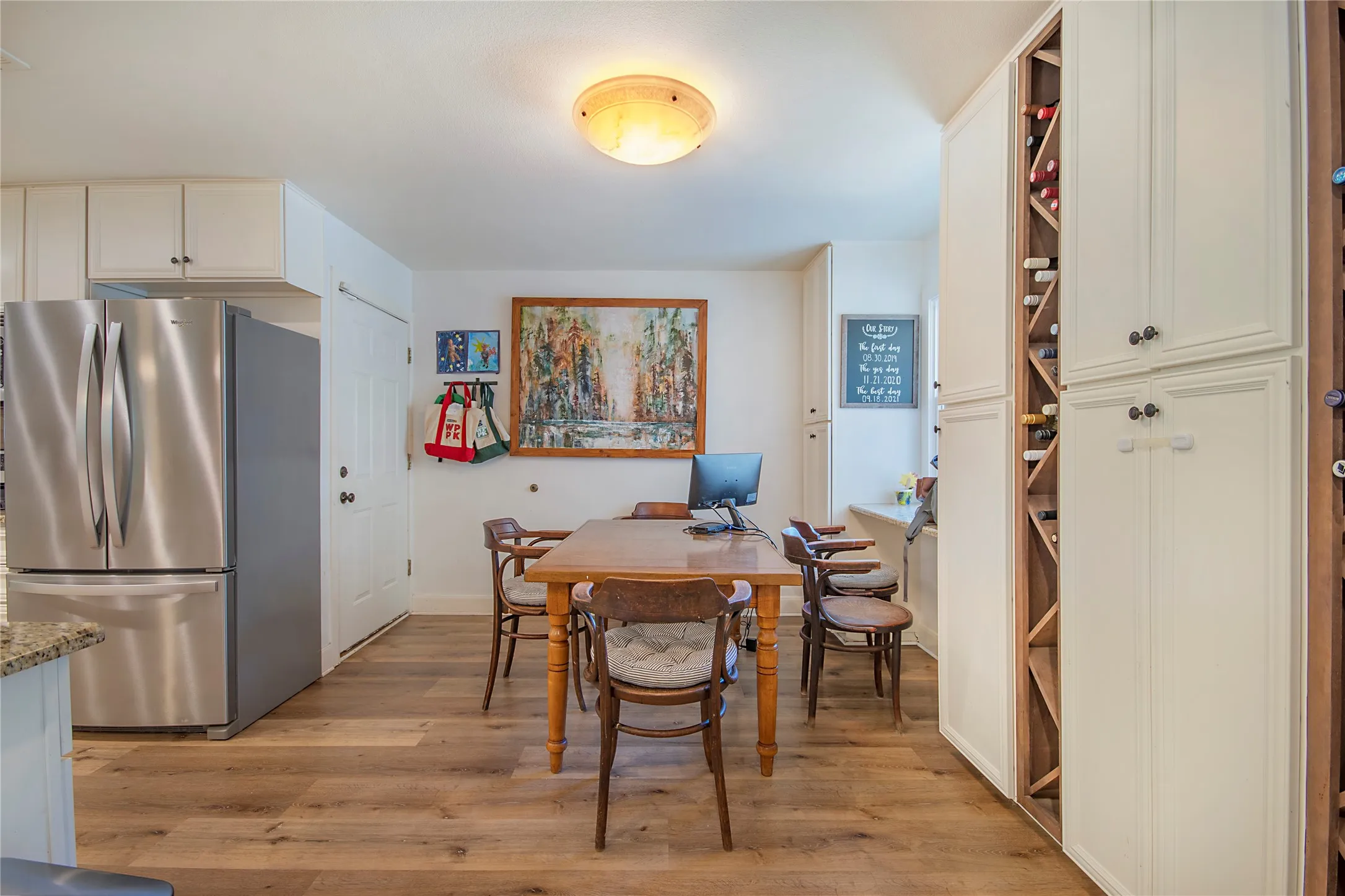 Wood-finish flooring, stainless steel refrigerator, white cabinetry, built-in wine storage, and a flush mount ceiling light