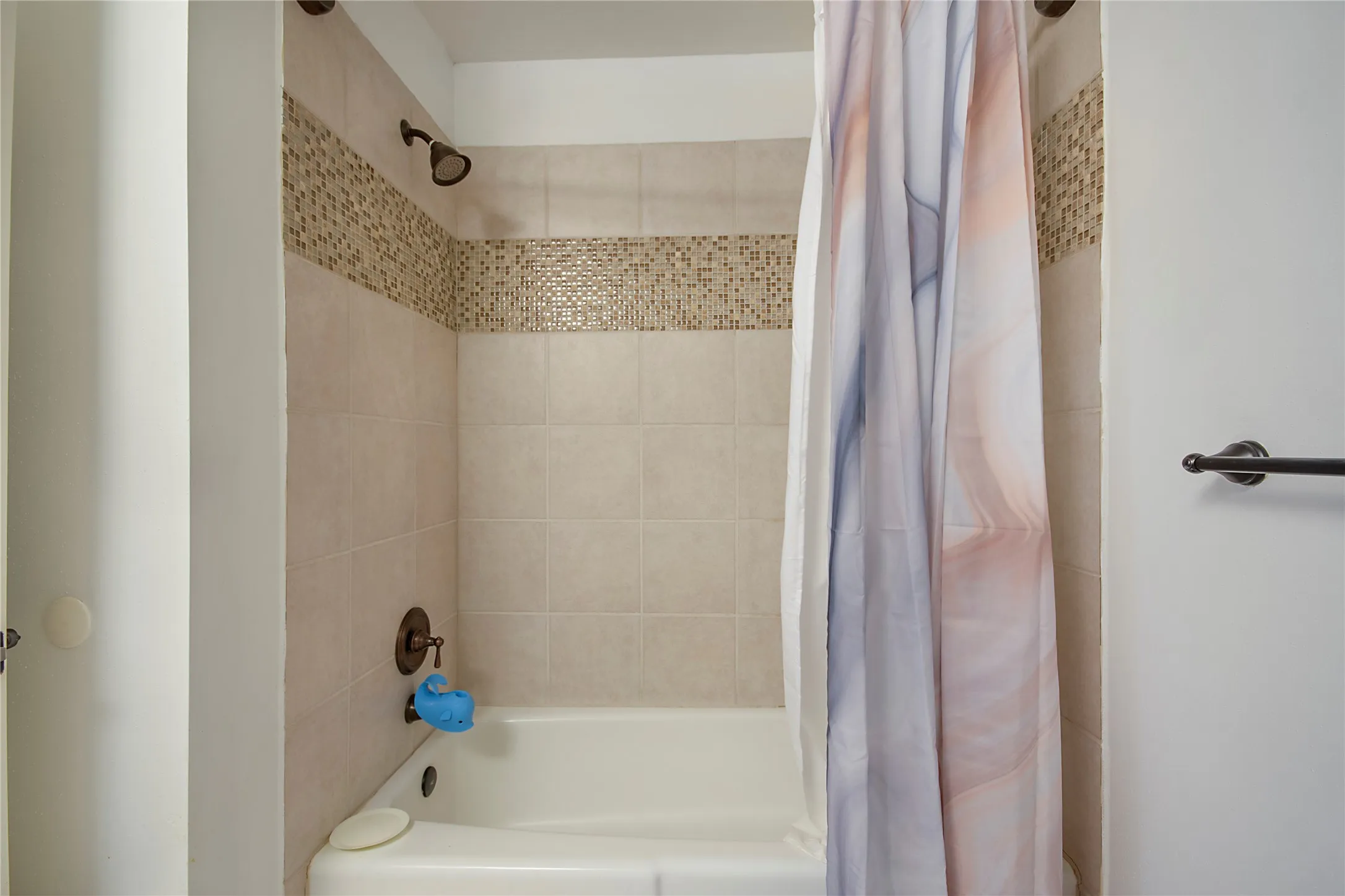 Bathtub with surrounding tile, decorative mosaic accent band, and bronze finish fixtures