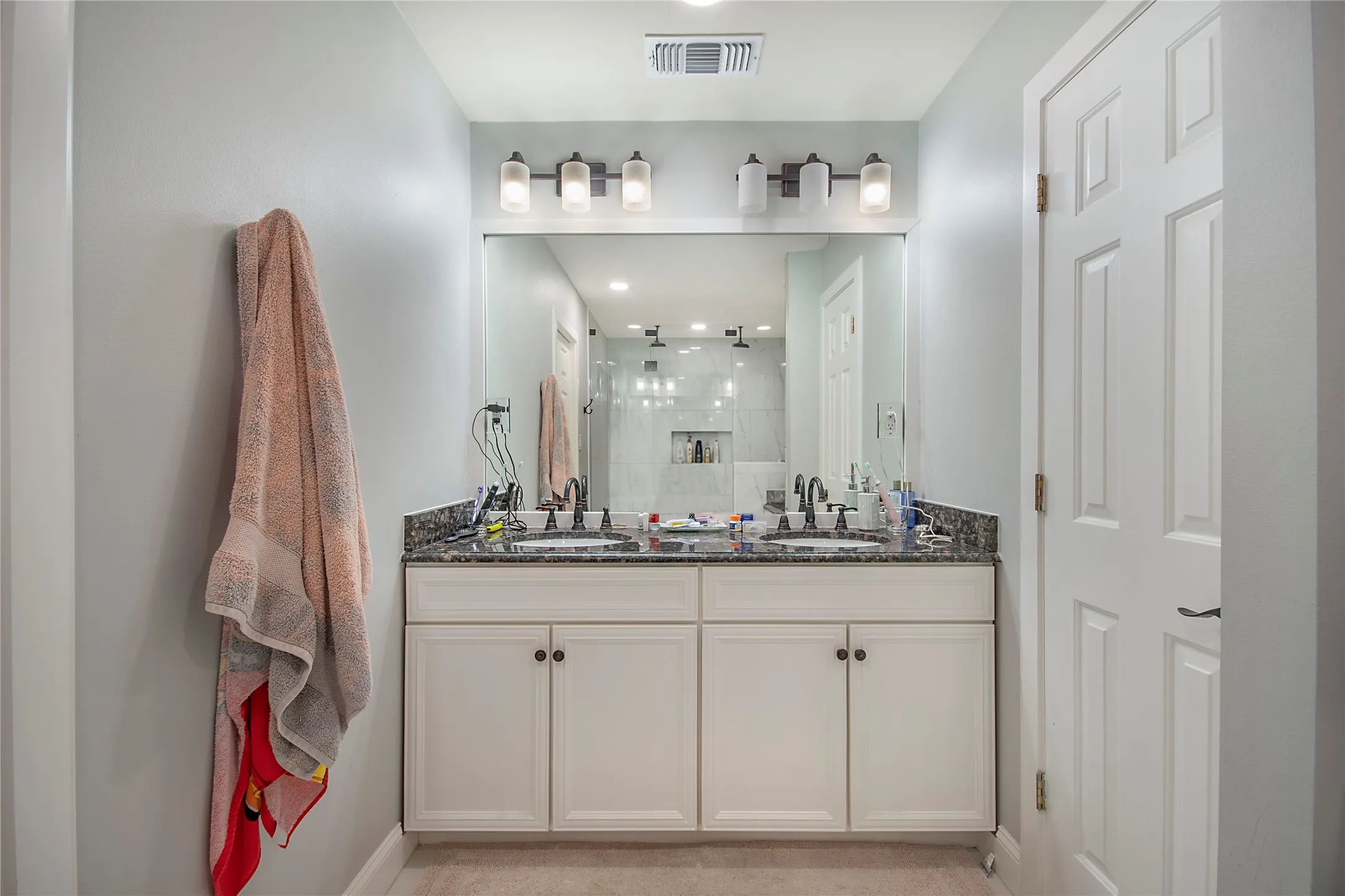 Double vanity with a dark countertop, undermount sinks, and wall-mounted light fixtures
