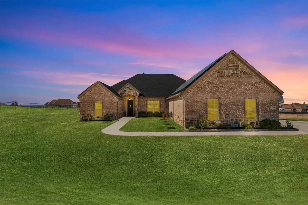 Beautiful twilight view highlighting the home's brick-and-stone exterior, inviting illuminated entryway, and expansive front lawn beneath a colorful evening sky.