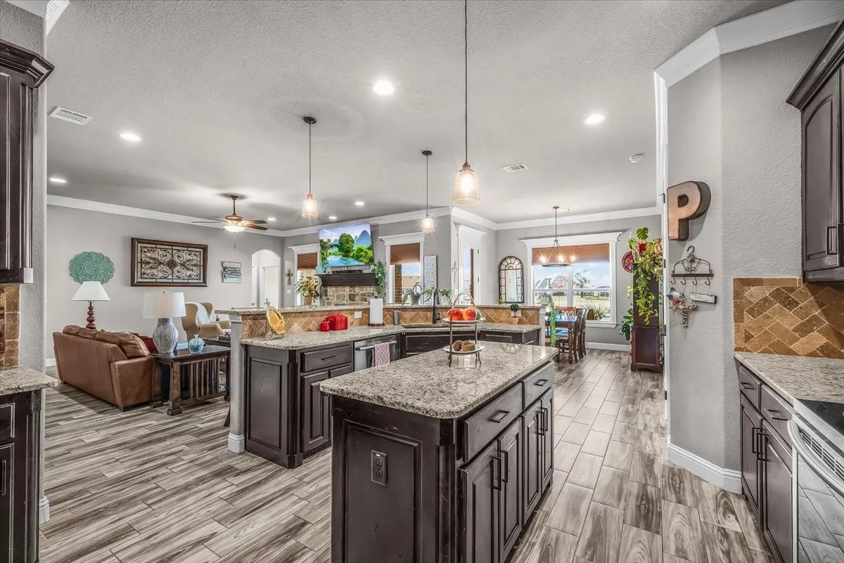 Kitchen: Standout wide-angle view showcases the spacious kitchen with dual granite-topped islands, extensive cabinetry, pendant lighting, and an open connection to the living and dining areas.