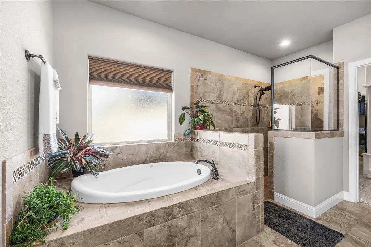 Primary Bathroom: Tile-surround soaking tub and separate walk-in shower create distinct bathing areas, complemented by natural light and decorative tile accents.