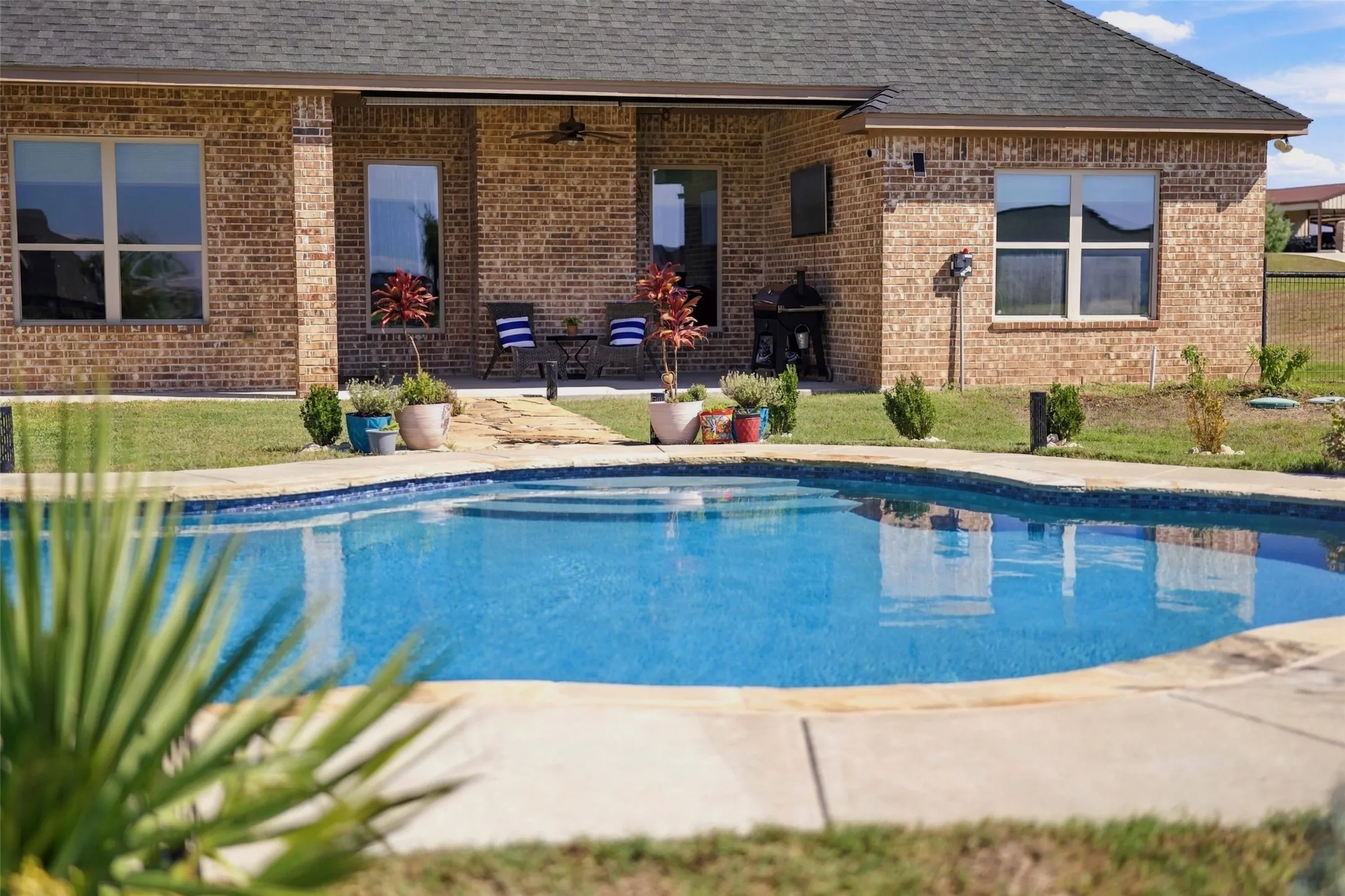 Sparkling in-ground pool featuring a curved design, wide concrete decking, and views of the expansive fenced backyard.