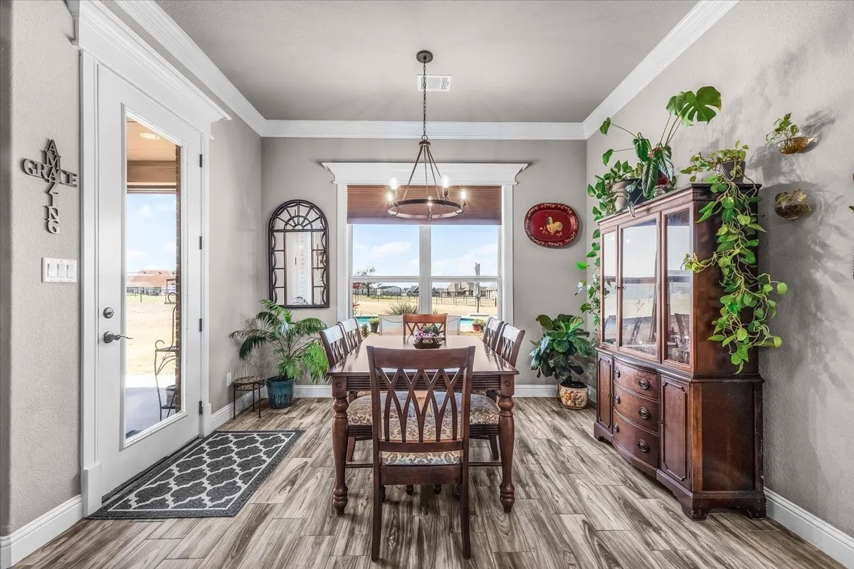 Dining Area: Bright dining space features a large window, crown molding, statement lighting, and direct access to the covered outdoor area.