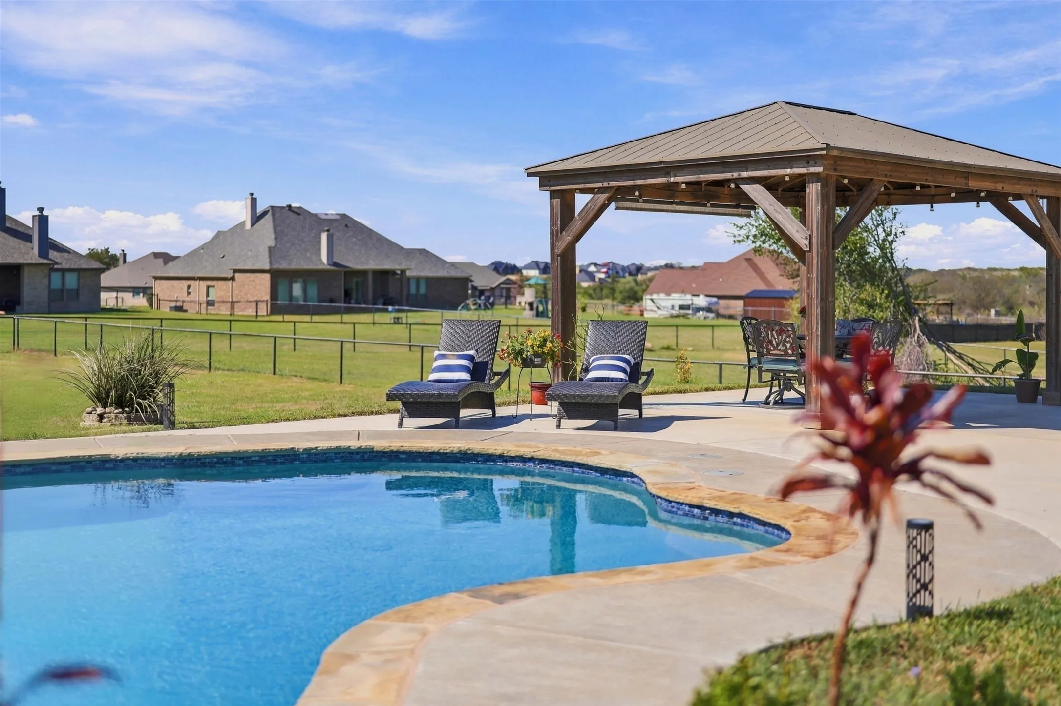 Curved swimming pool with concrete decking, a wooden pergola, and a fenced yard