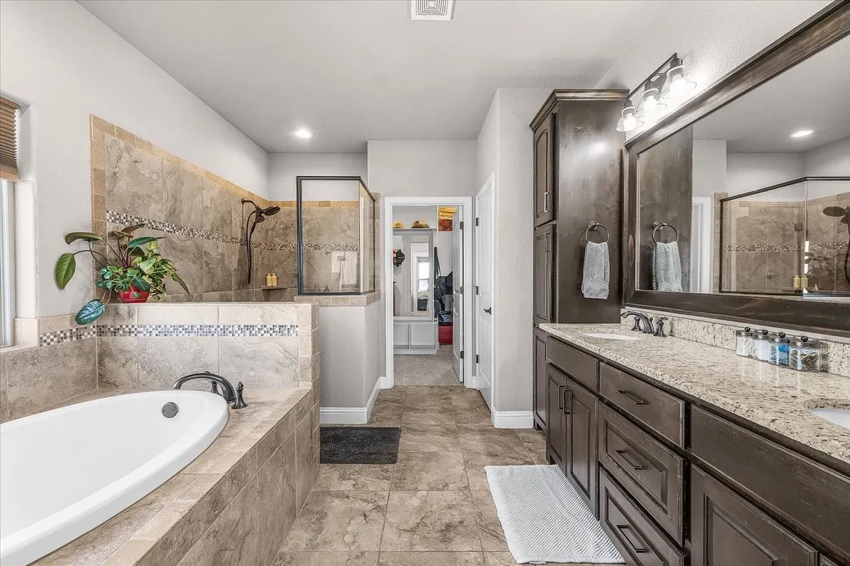 Primary Bathroom: Spacious en-suite bath features a dual-sink granite vanity, dark wood cabinetry, soaking tub, separate tiled shower, and coordinated tile flooring.