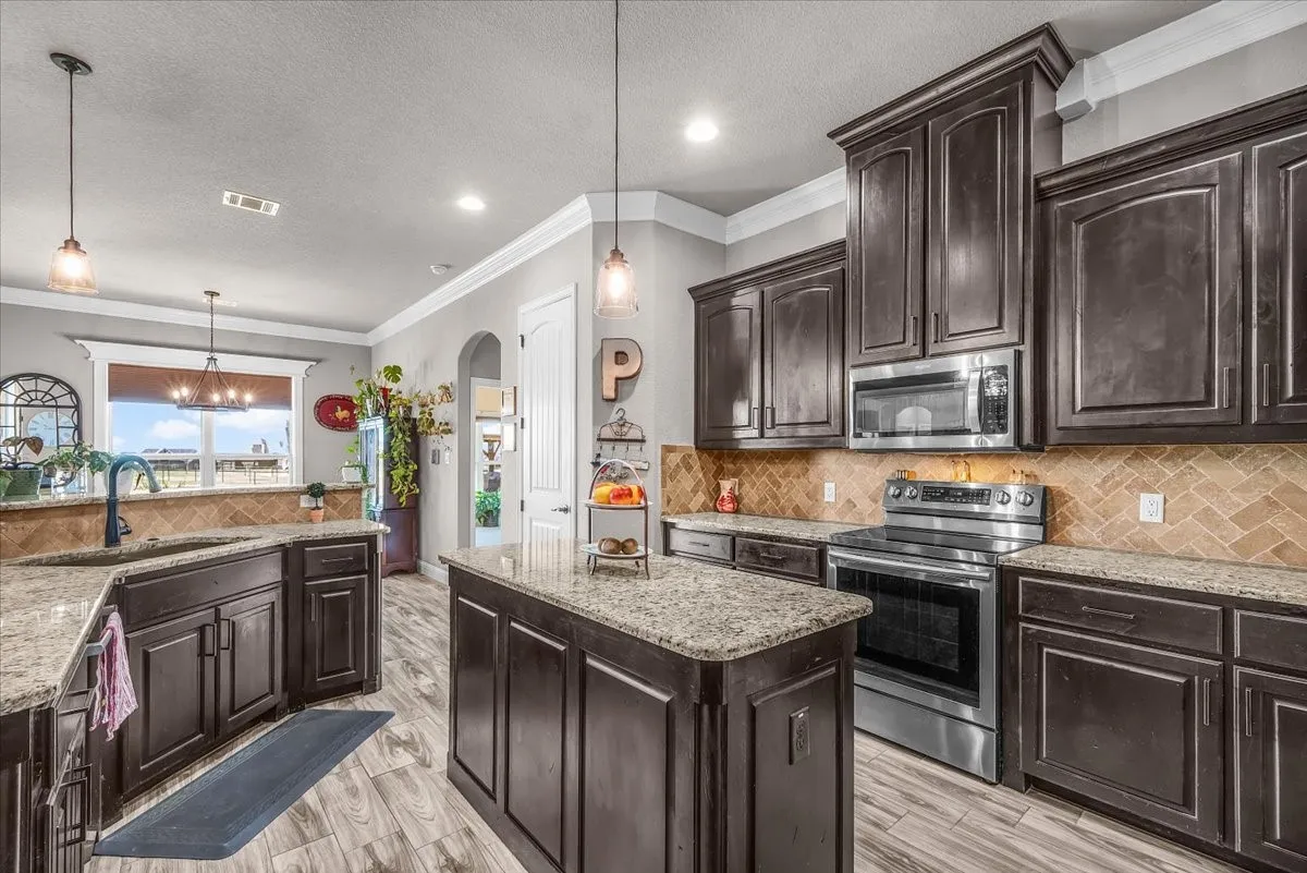 Kitchen: Generous cabinetry and counter space surround the center island, complemented by granite surfaces, stainless steel appliances, tile backsplash, and pendant lighting.