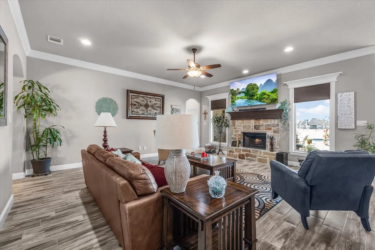 Living Room: Bright living room features a floor-to-ceiling stone fireplace, large windows, crown molding, and durable wood-look flooring.