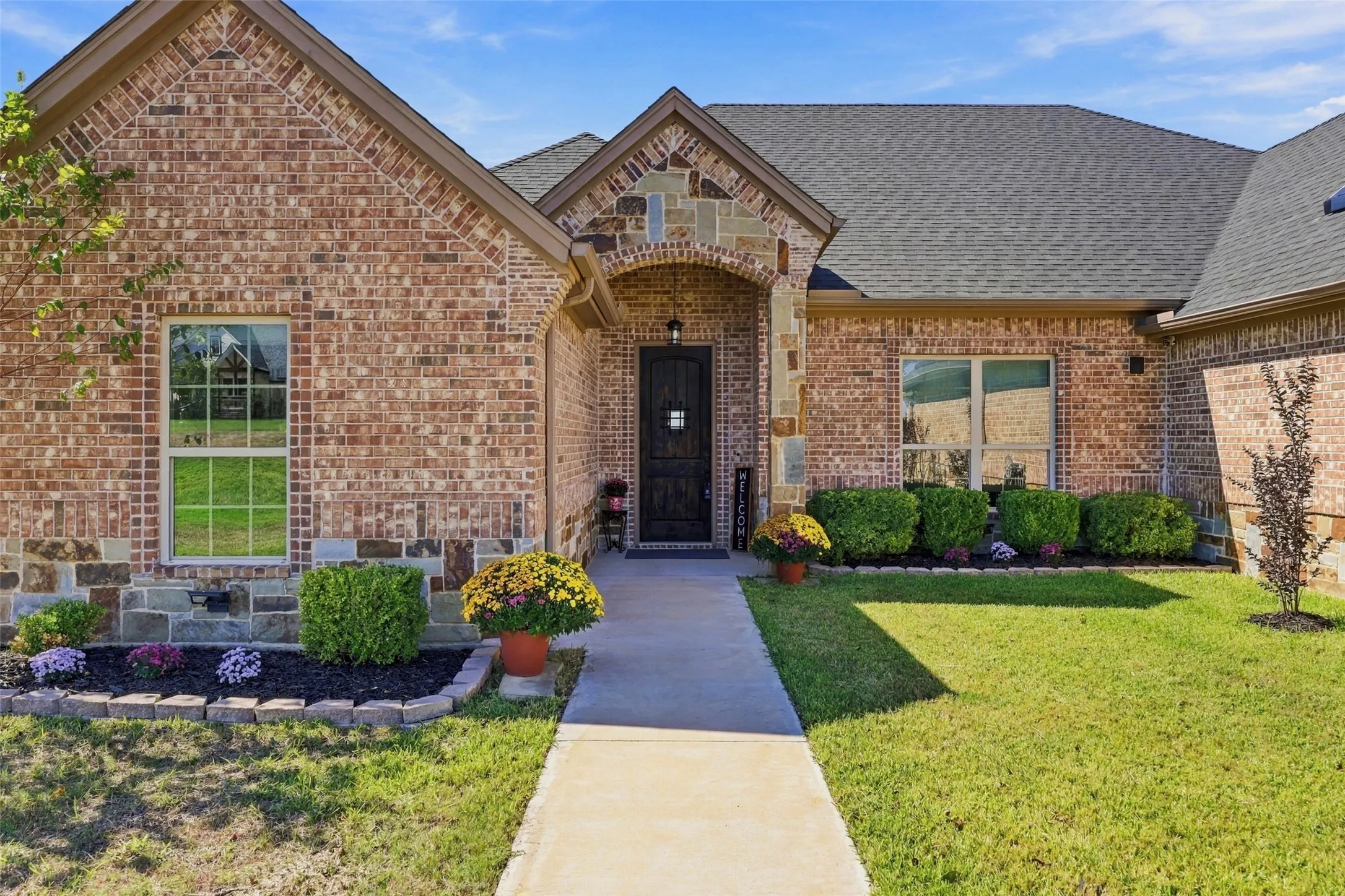 Welcoming covered entry framed by beautiful stonework, decorative brick detailing, and colorful landscaping.