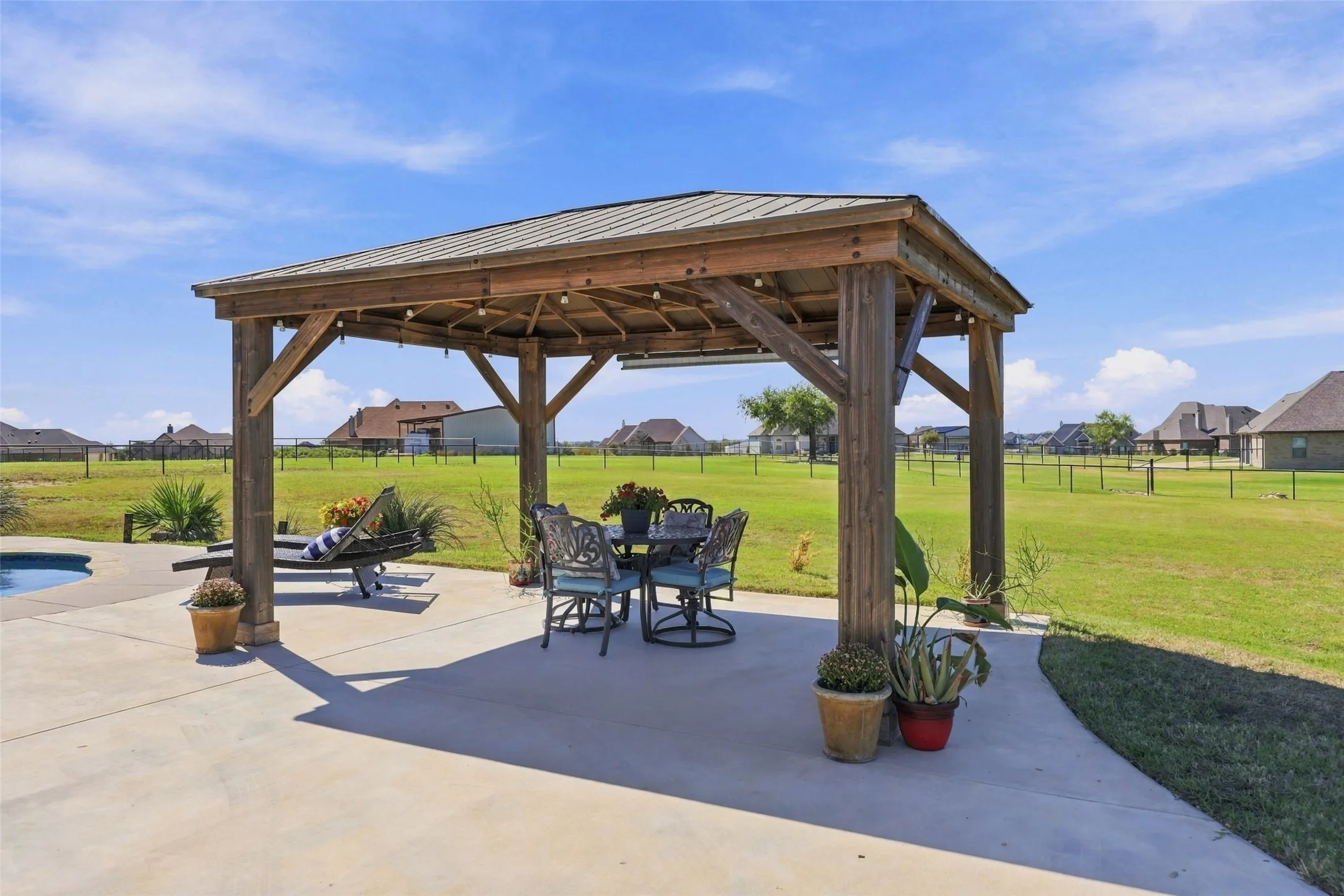 Beautiful wood-framed pavilion with a metal roof, shaded dining area, and decorative lighting, offering a welcoming space to relax or entertain beside the pool.