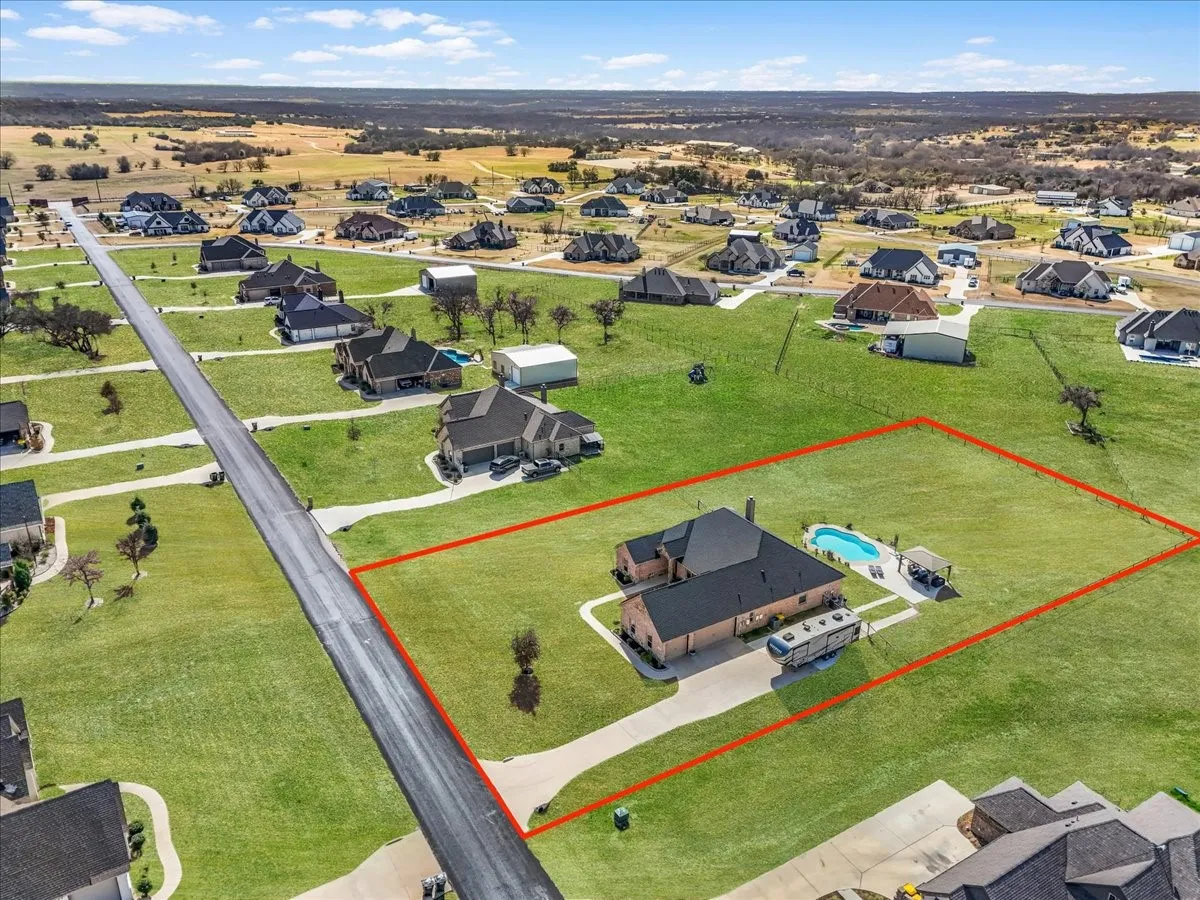 Expansive property featuring a brick exterior residence, a paved driveway, a swimming pool, and a detached patio cover