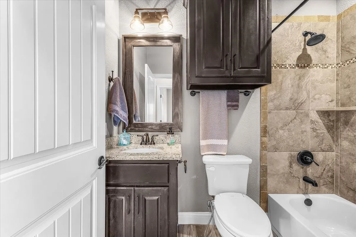 5. Bathroom: Full bathroom features a granite-topped vanity, dark wood cabinetry, and a tub-shower combination with decorative tile surround.