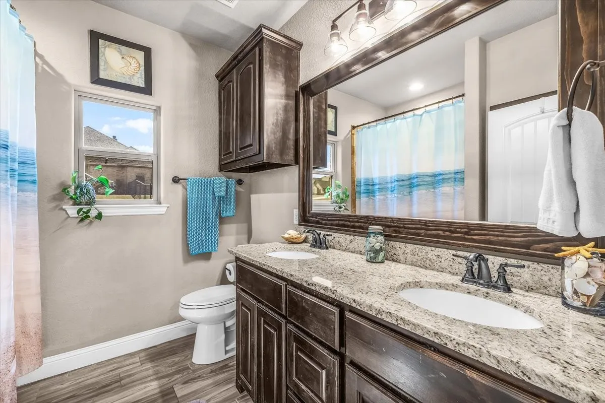 Bathroom: Well-appointed bathroom features a dual-sink granite vanity, dark wood cabinetry, an oversized framed mirror, and natural light from the window.