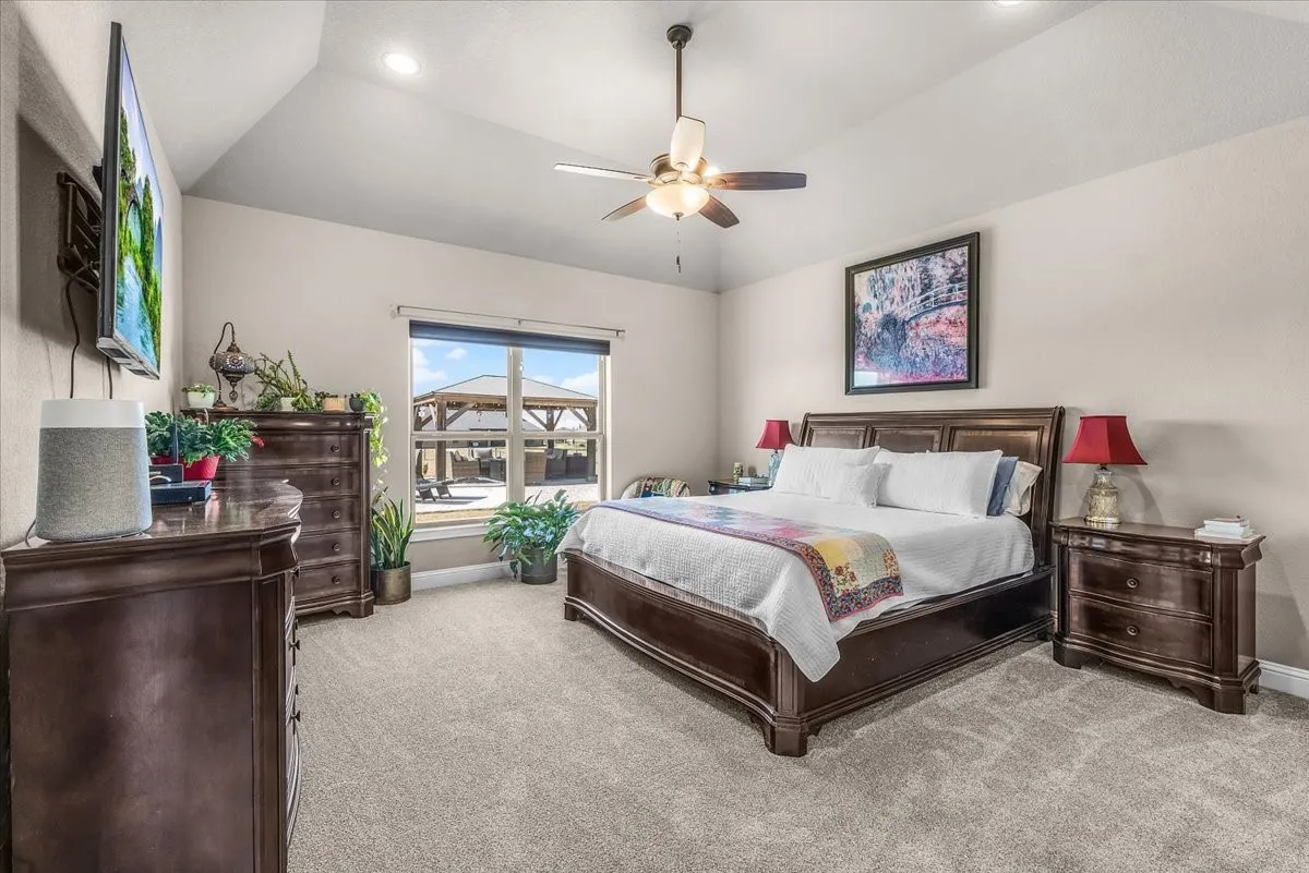 Primary Bedroom: Bright primary suite offers generous floor space, a vaulted ceiling, ceiling fan, and a large window overlooking the outdoor living area.
