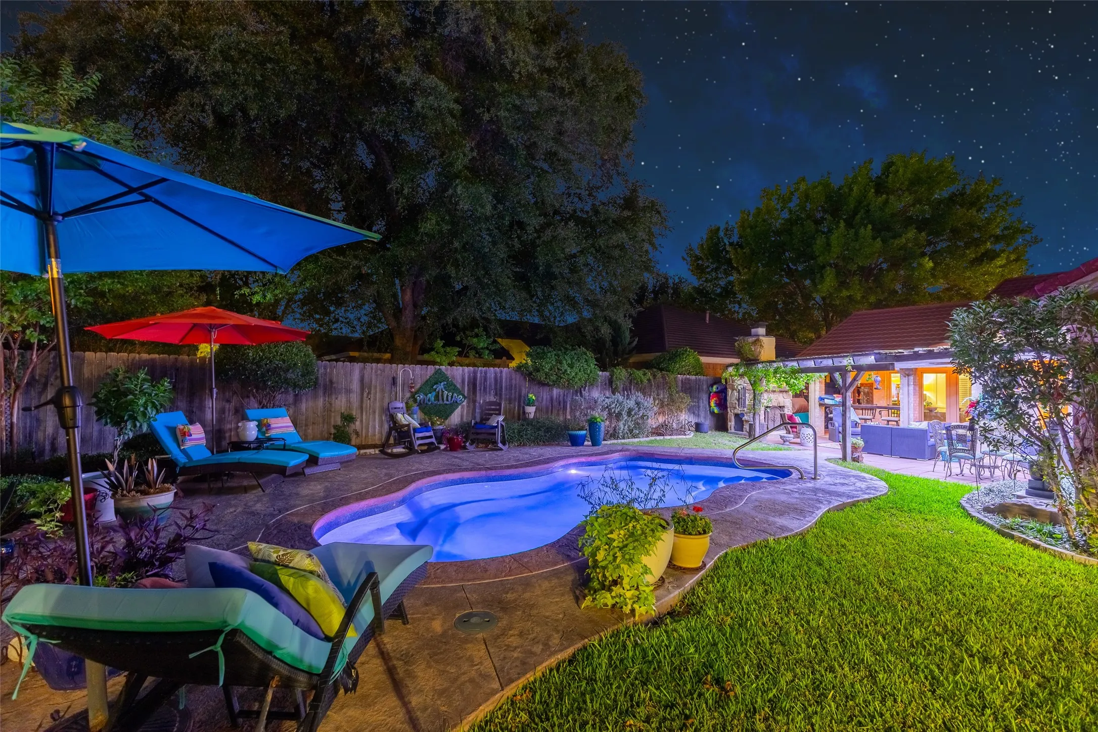 Curved swimming pool with integrated spa, concrete decking, manicured lawn, and a covered patio area