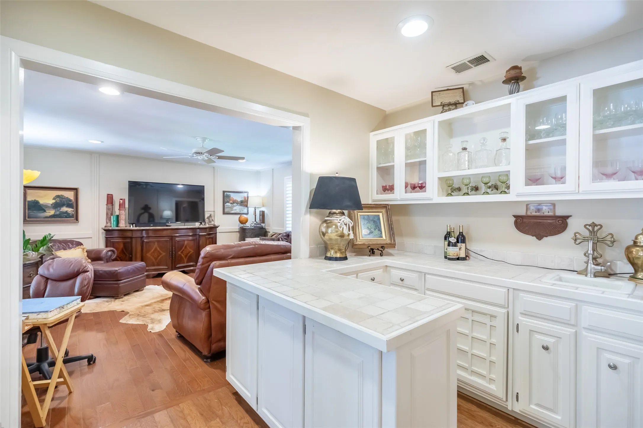 Wet bar featuring white cabinetry, glass-front upper cabinets, and a tile countertop