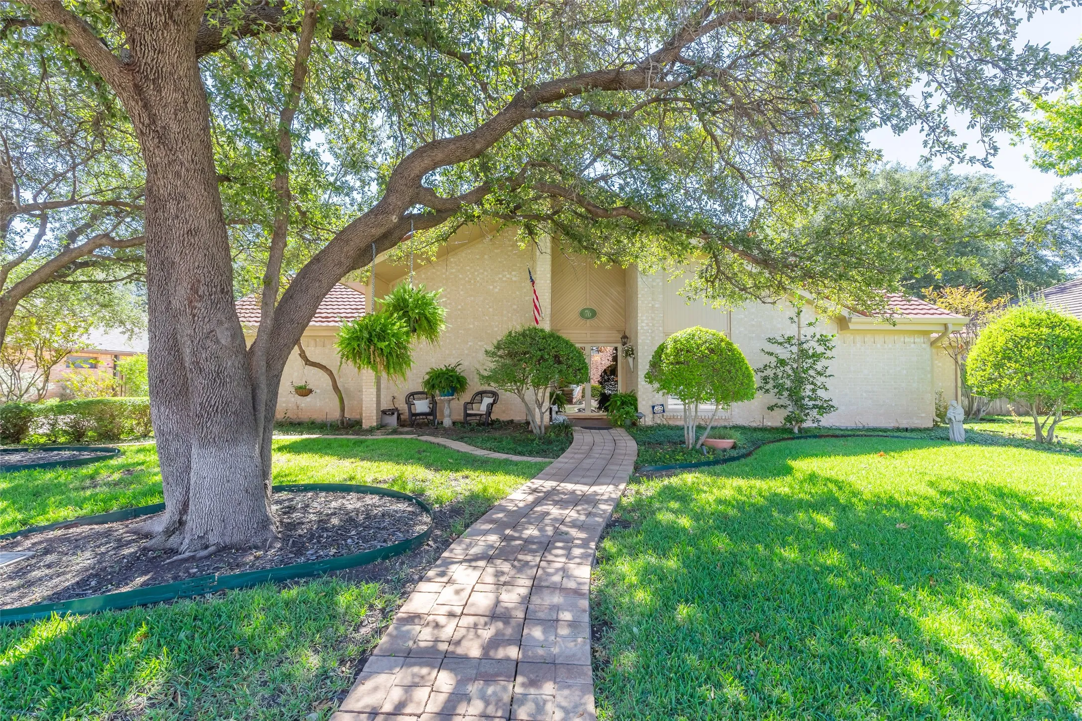 Mature shade tree anchors the front grounds, framing a brick paver walkway leading to the residence