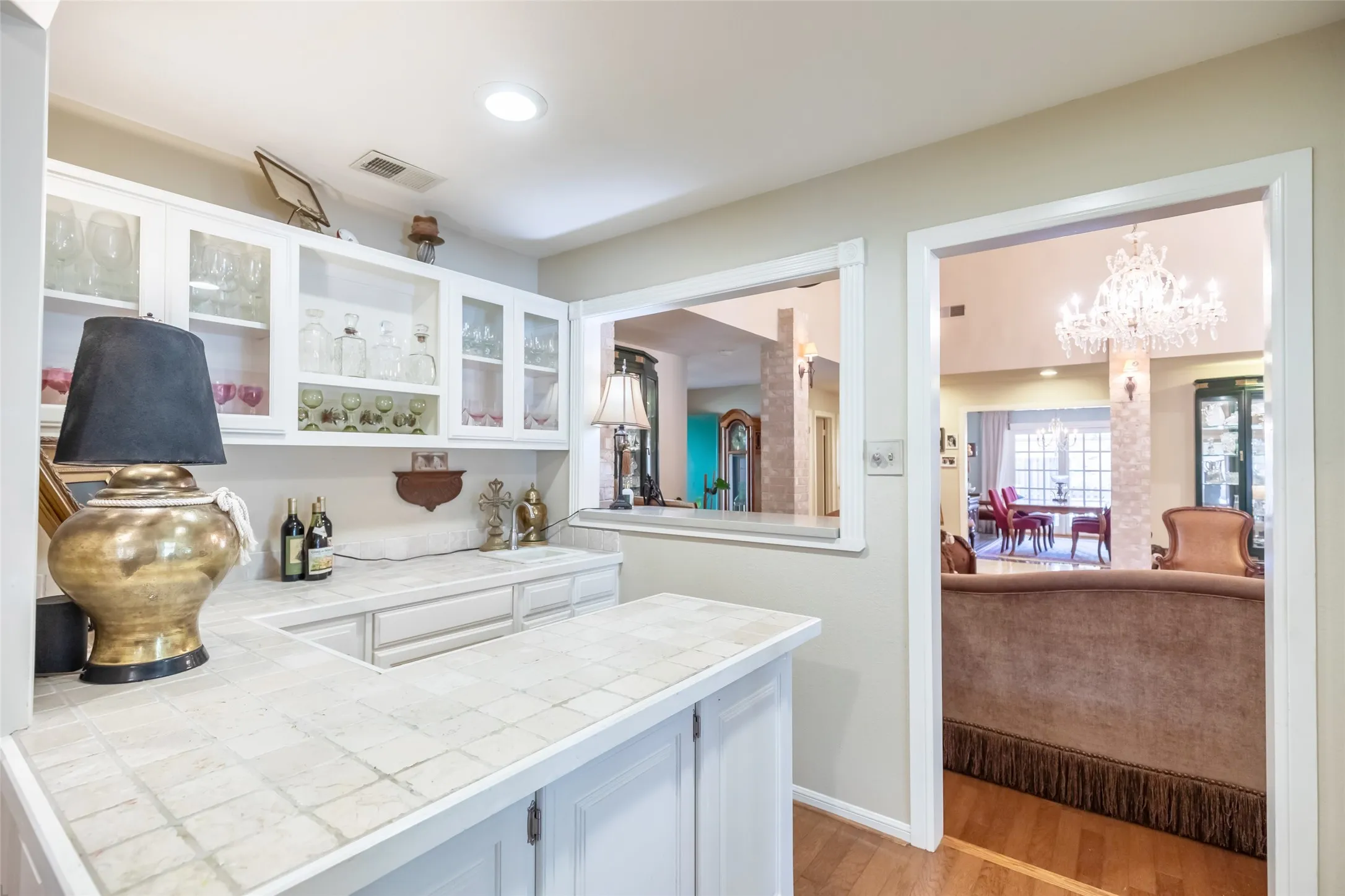 Built-in wet bar featuring white cabinetry, glass-front upper cabinets, and a tiled countertop