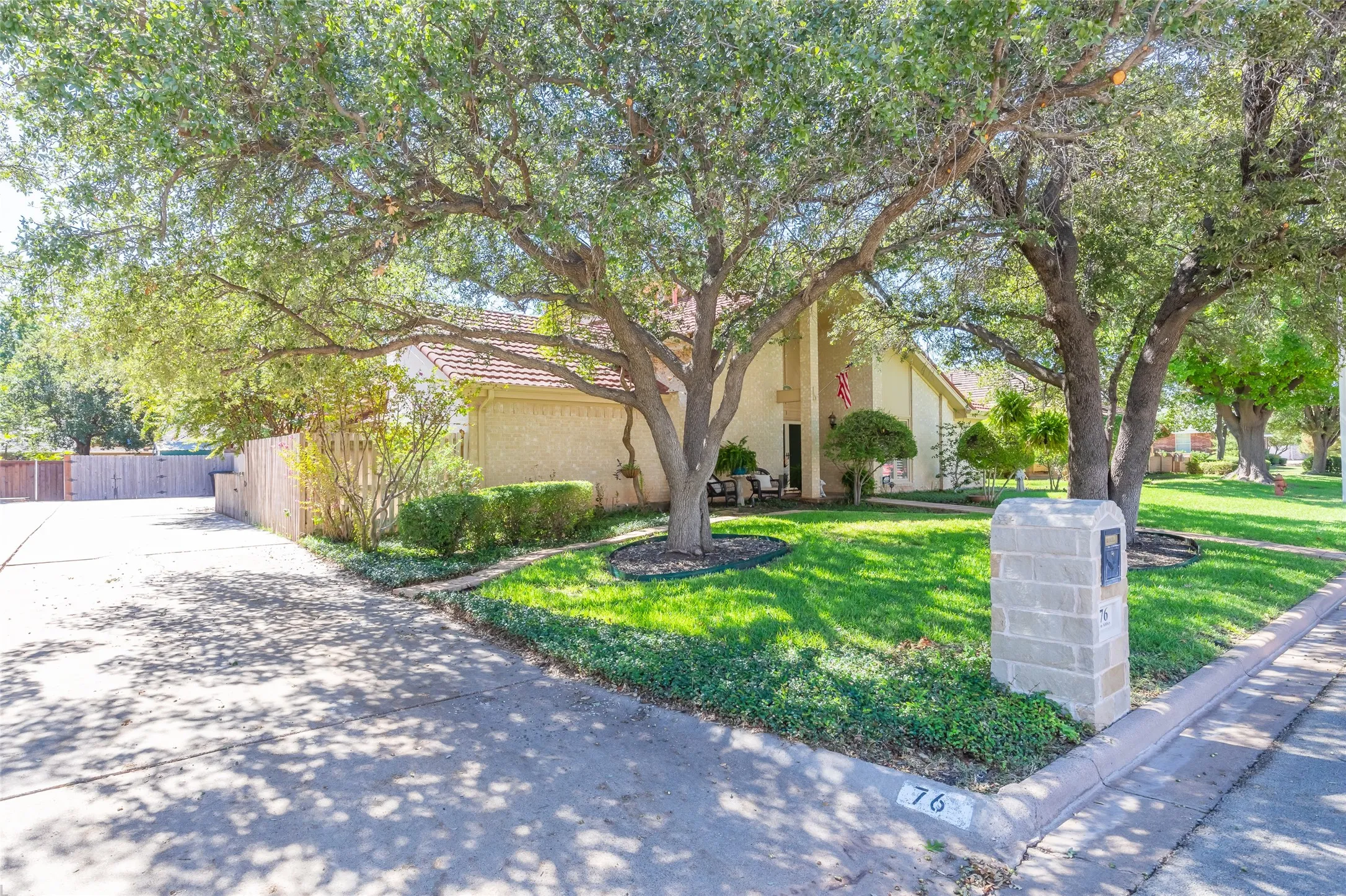 Stucco exterior with a tile roof, mature trees, a manicured lawn, a concrete driveway, and a stone-clad mailbox