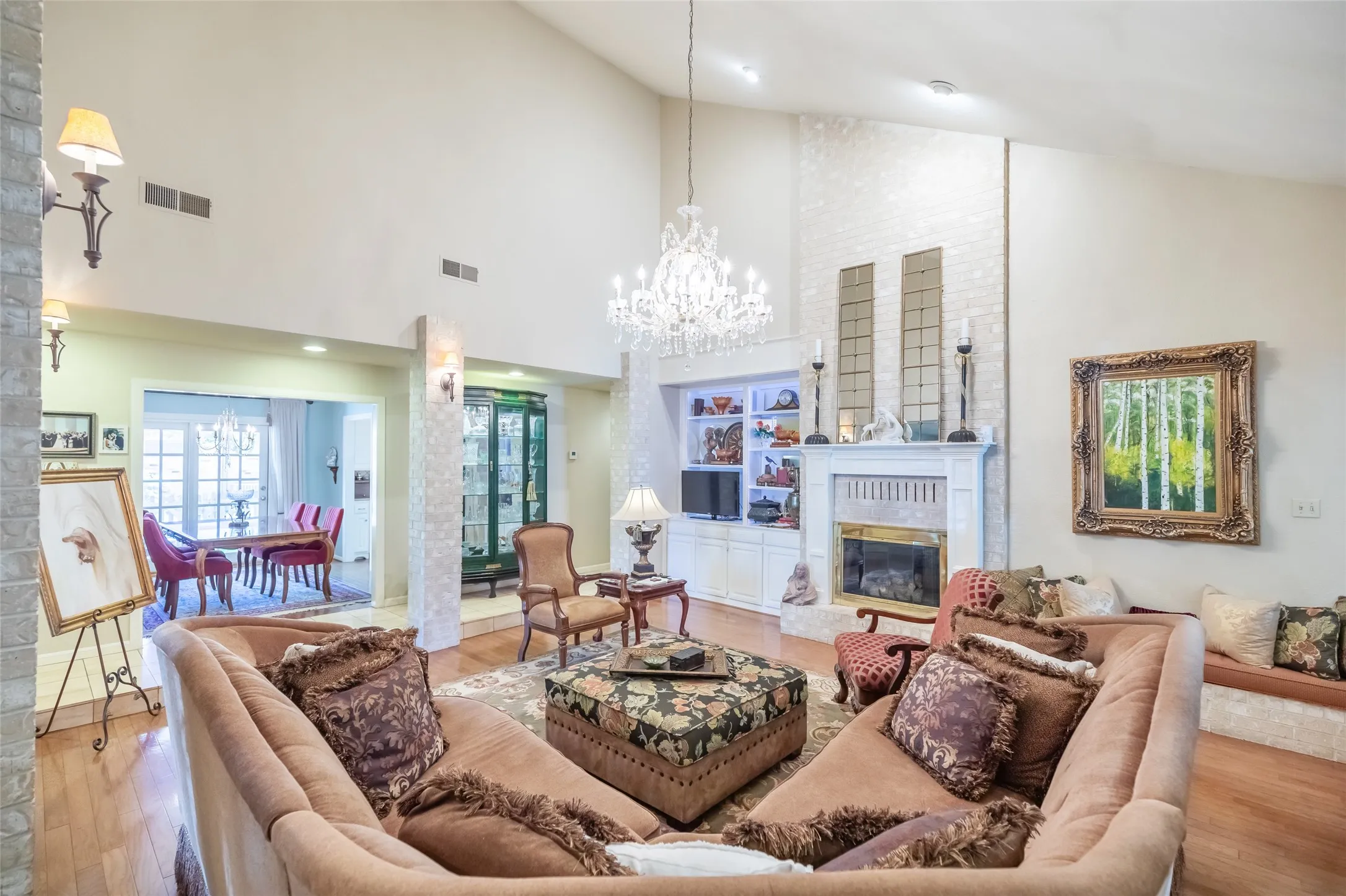 Vaulted ceilings with a prominent chandelier, brick-finish fireplace, built-in display shelving, and wood-finish flooring