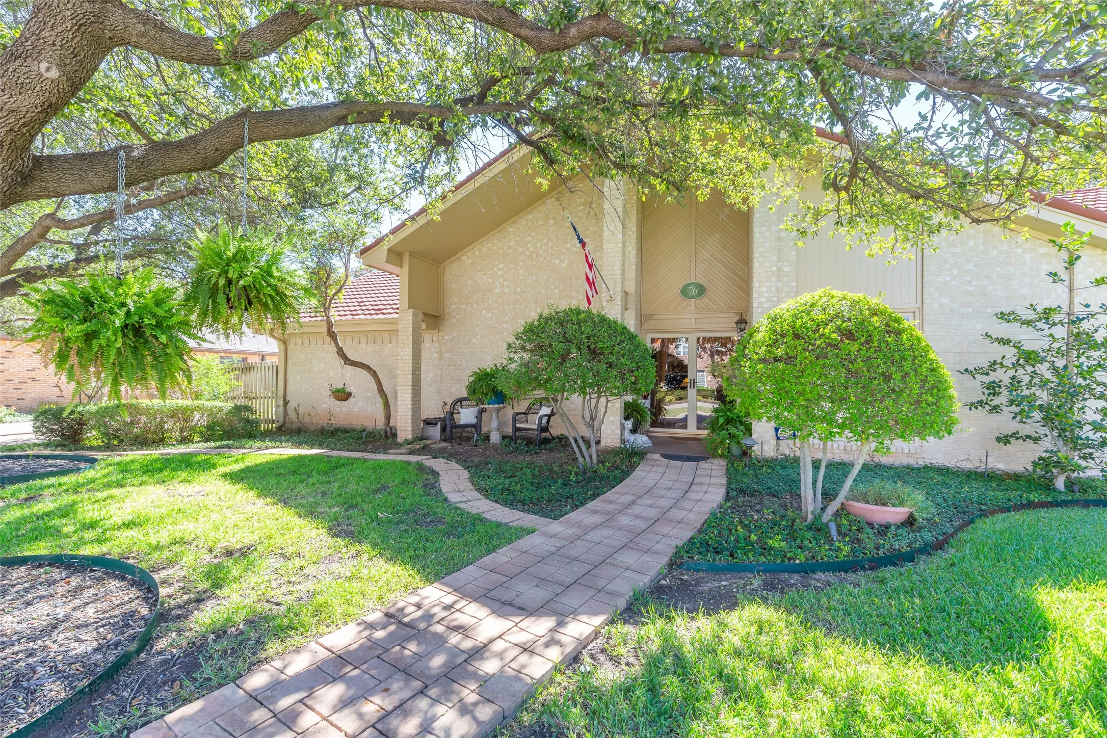 Paved entryway leading to a double-door entrance, complemented by a large mature tree and varied landscaping