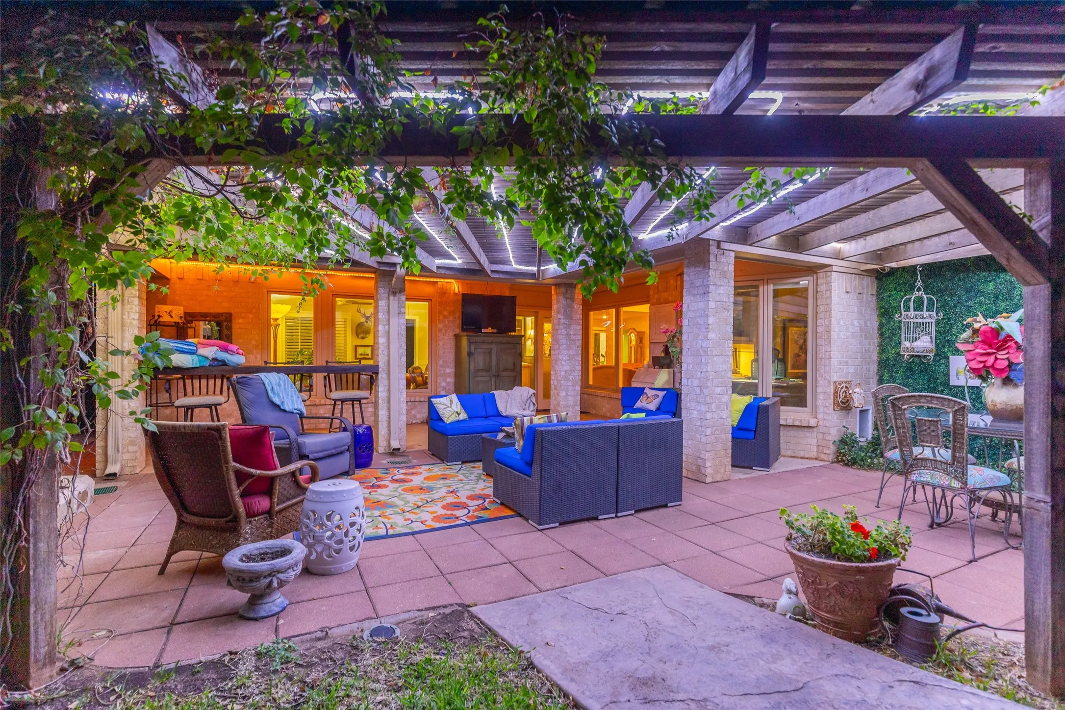 Expansive patio featuring a wooden pergola, lush green foliage, and tile flooring