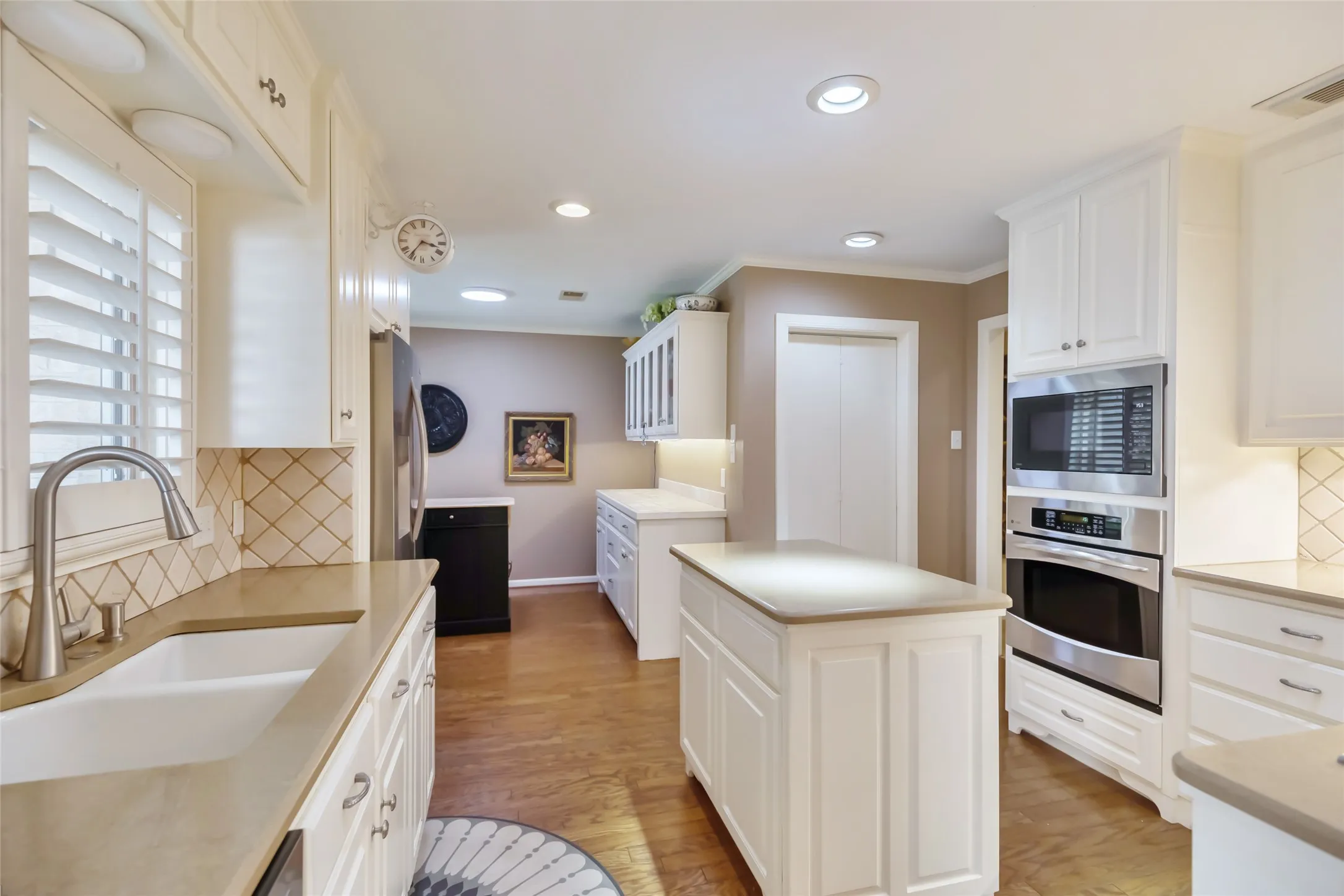 White cabinetry, stone countertops, stainless steel appliances, wood-finish flooring, and a central island