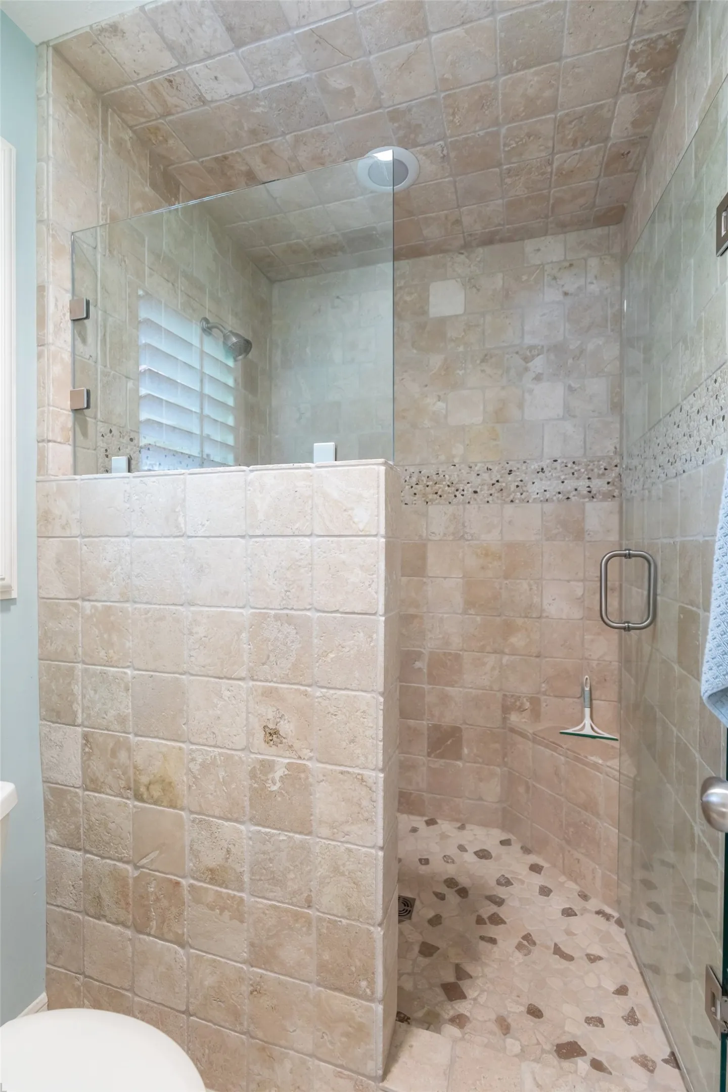 Walk-in shower with full tile surround, decorative mosaic accent band, stone pebble-finish shower pan, and a glass enclosure