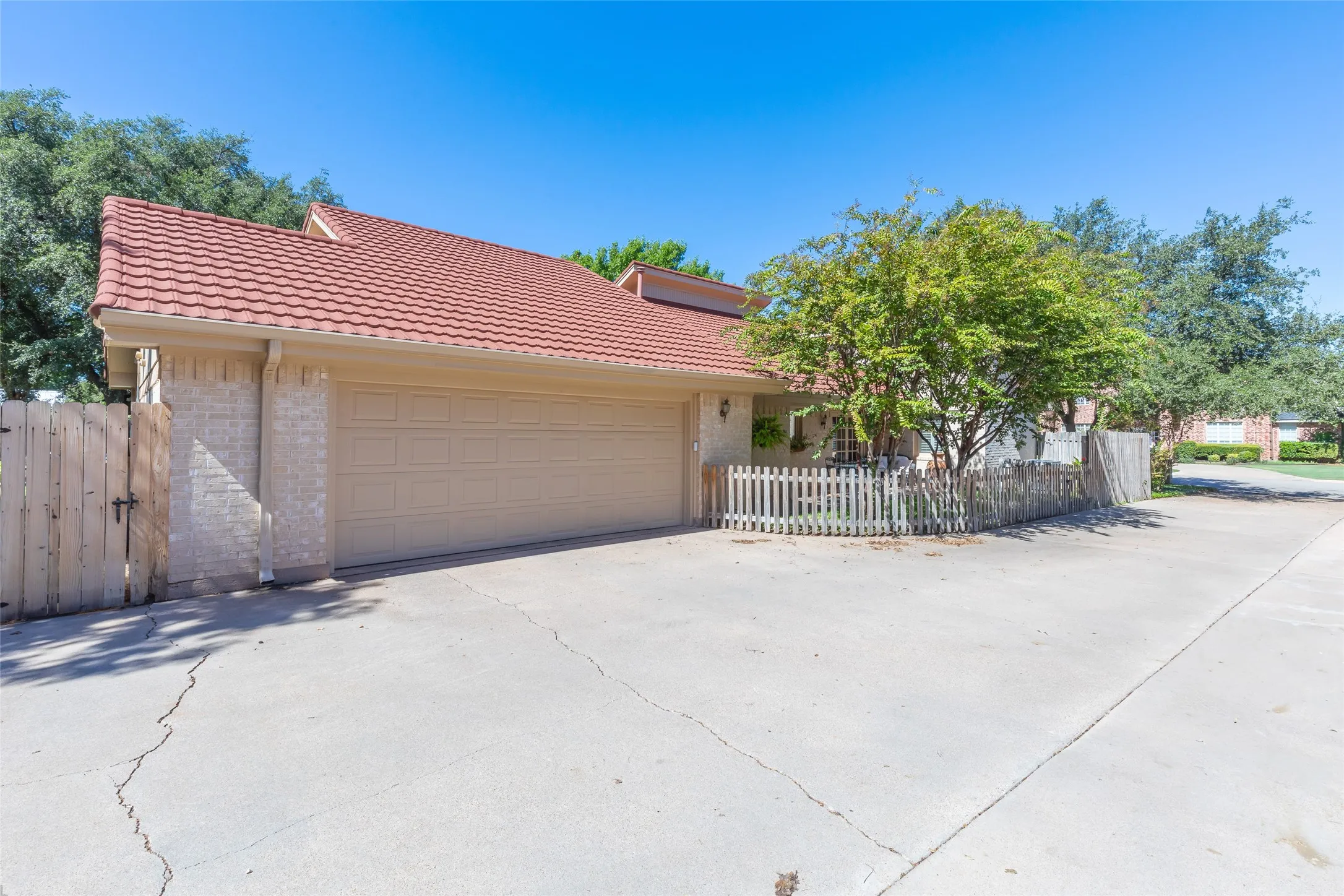Attached two-car garage with a panel door, red tile roofing, and a front patio with a white picket fence