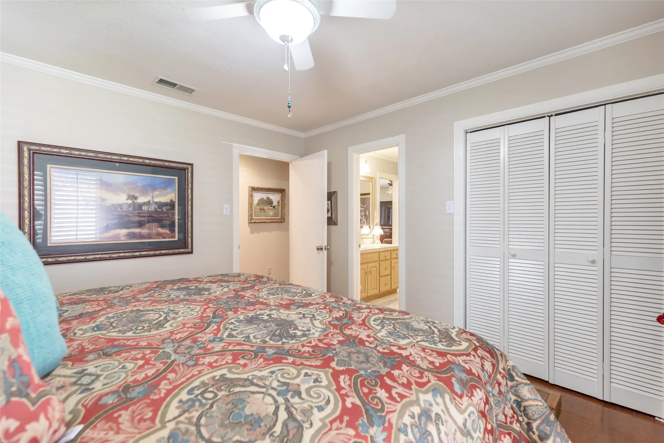 White louvered bi-fold closet doors, ceiling fan with integrated lighting, crown molding, and wood-finish flooring