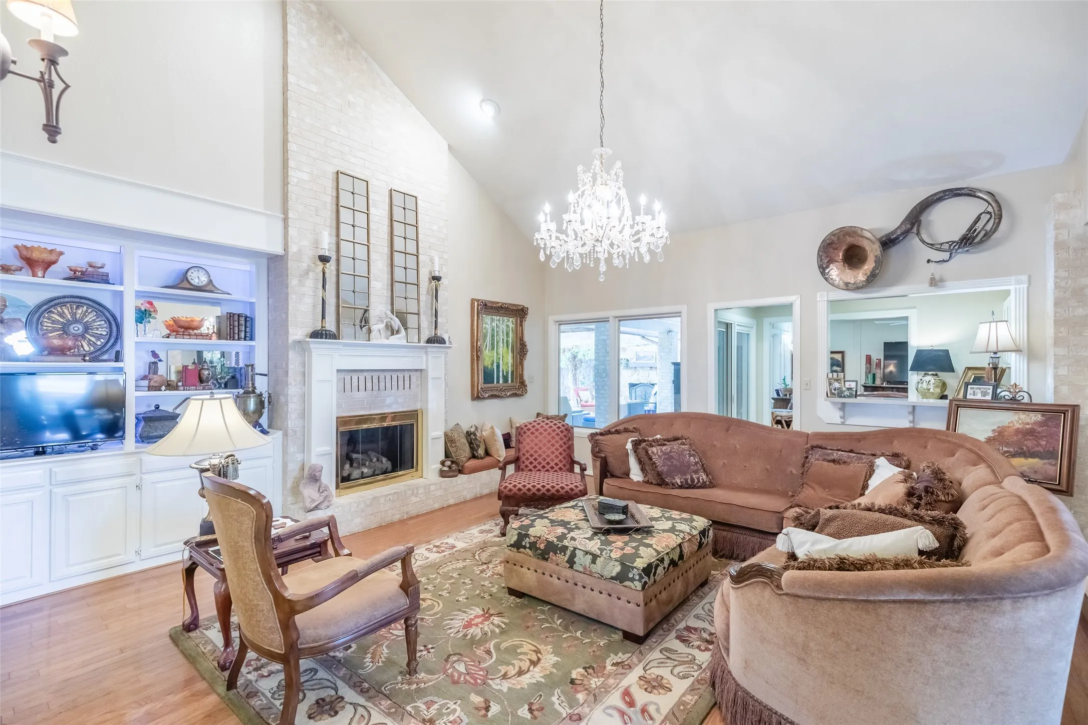 Vaulted ceiling, illuminated built-in cabinetry, brick-clad fireplace with mantel, chandelier, and wood-finish flooring