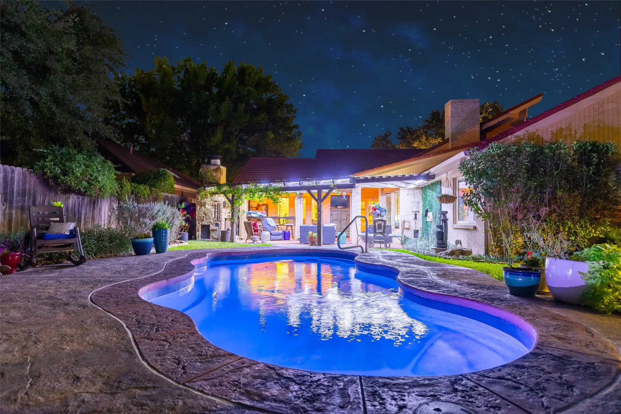 Freeform swimming pool with stamped concrete decking, covered patio, and exterior lighting