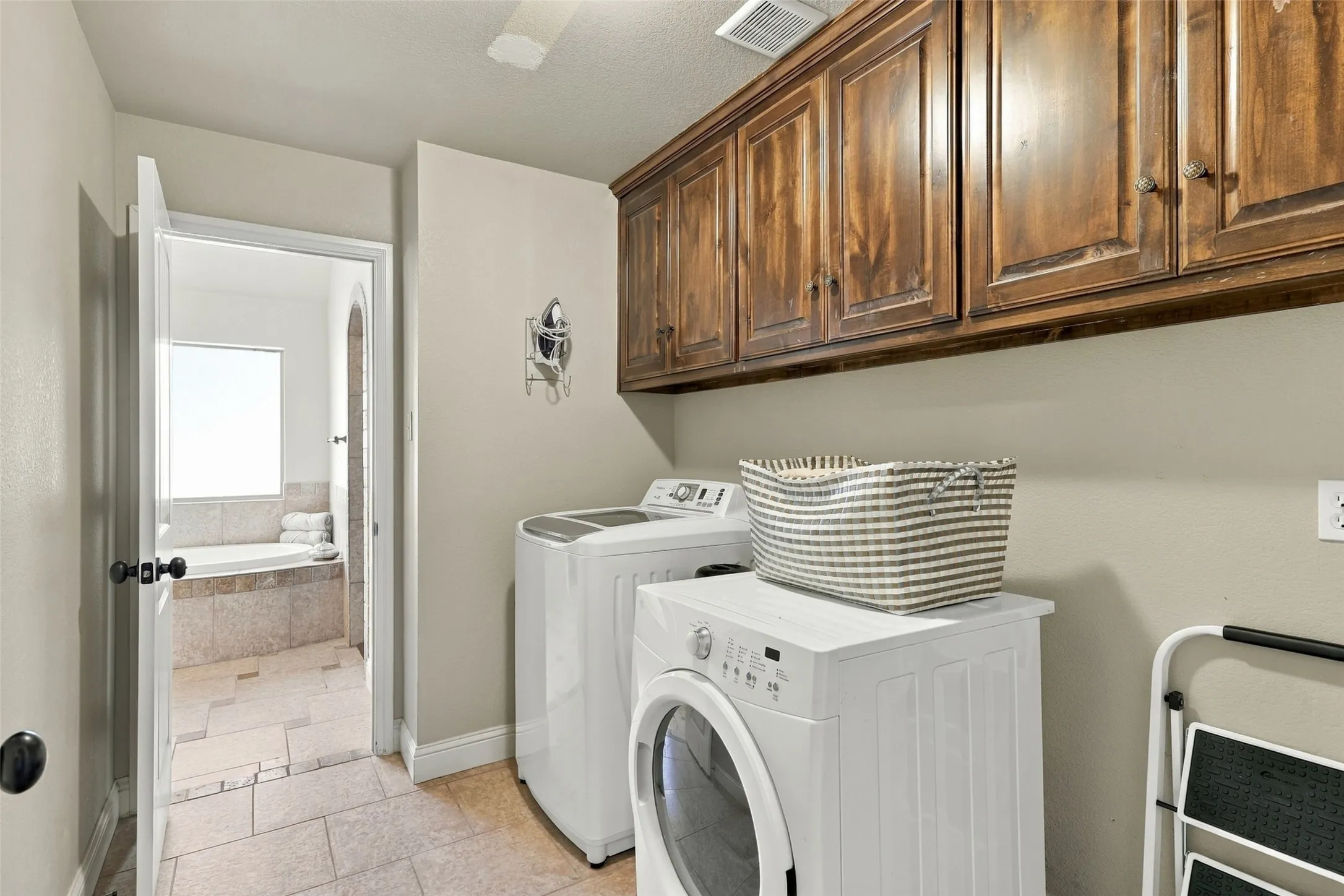 Laundry Room: Convenient laundry area features overhead wood cabinetry, tile flooring, and space for a full-size washer and dryer.