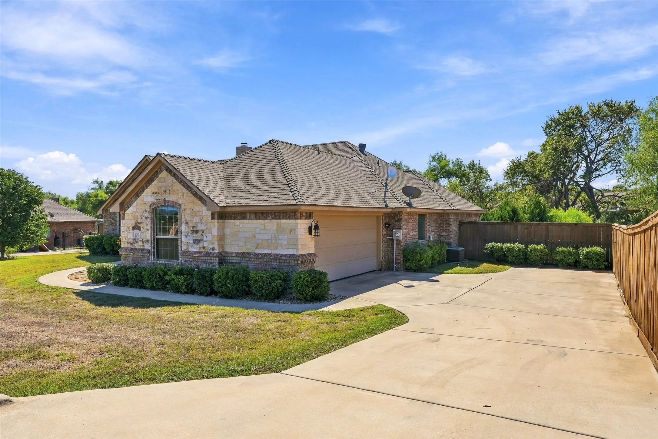Garage & Driveway: Side-entry garage features an expansive concrete driveway, brick and stone exterior detailing, and wood privacy fencing.