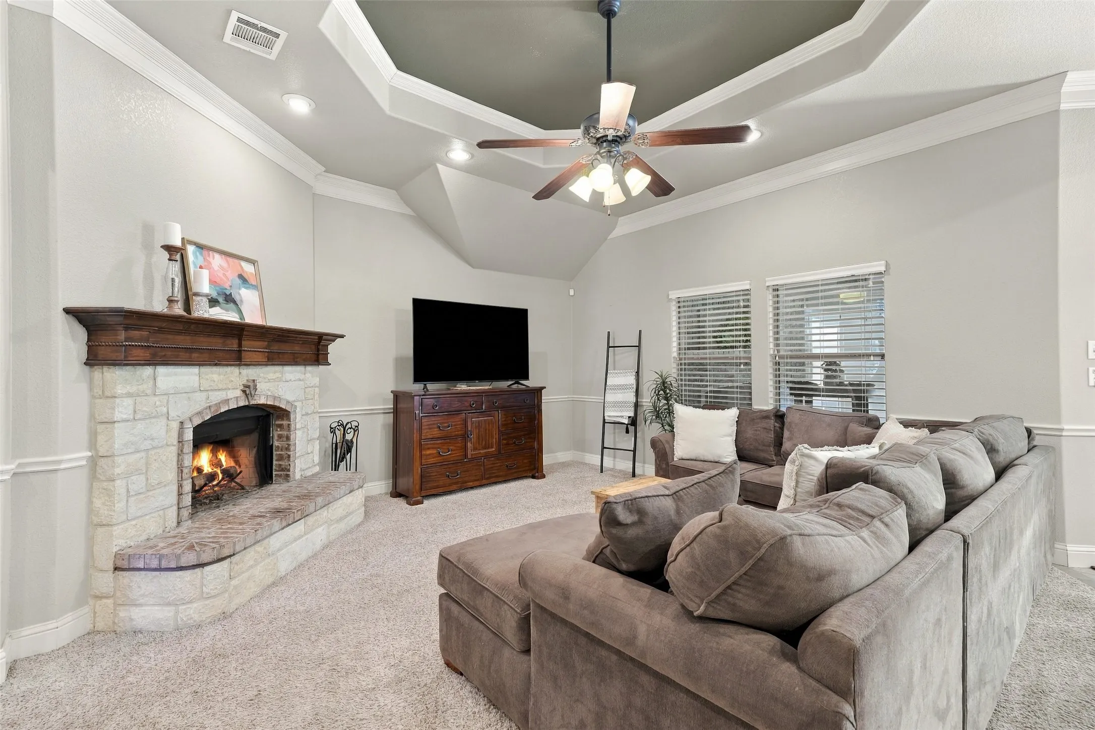 Living Room: Inviting living space features a floor-to-ceiling stone fireplace with wood mantel, elegant tray ceiling, crown molding, and abundant natural light.