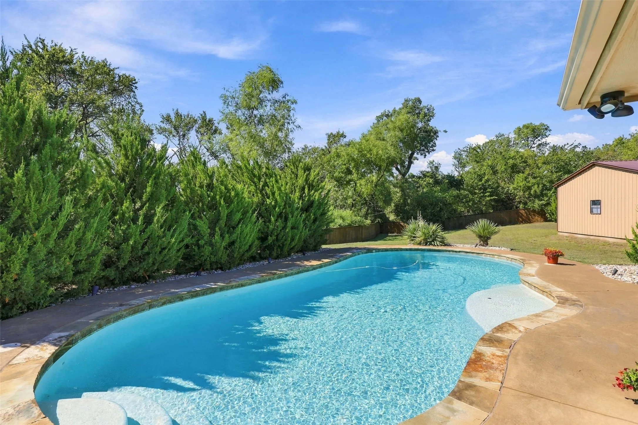 Swimming Pool: Sparkling freeform pool features a shallow entry area, surrounding concrete decking, and mature landscaping for added privacy.