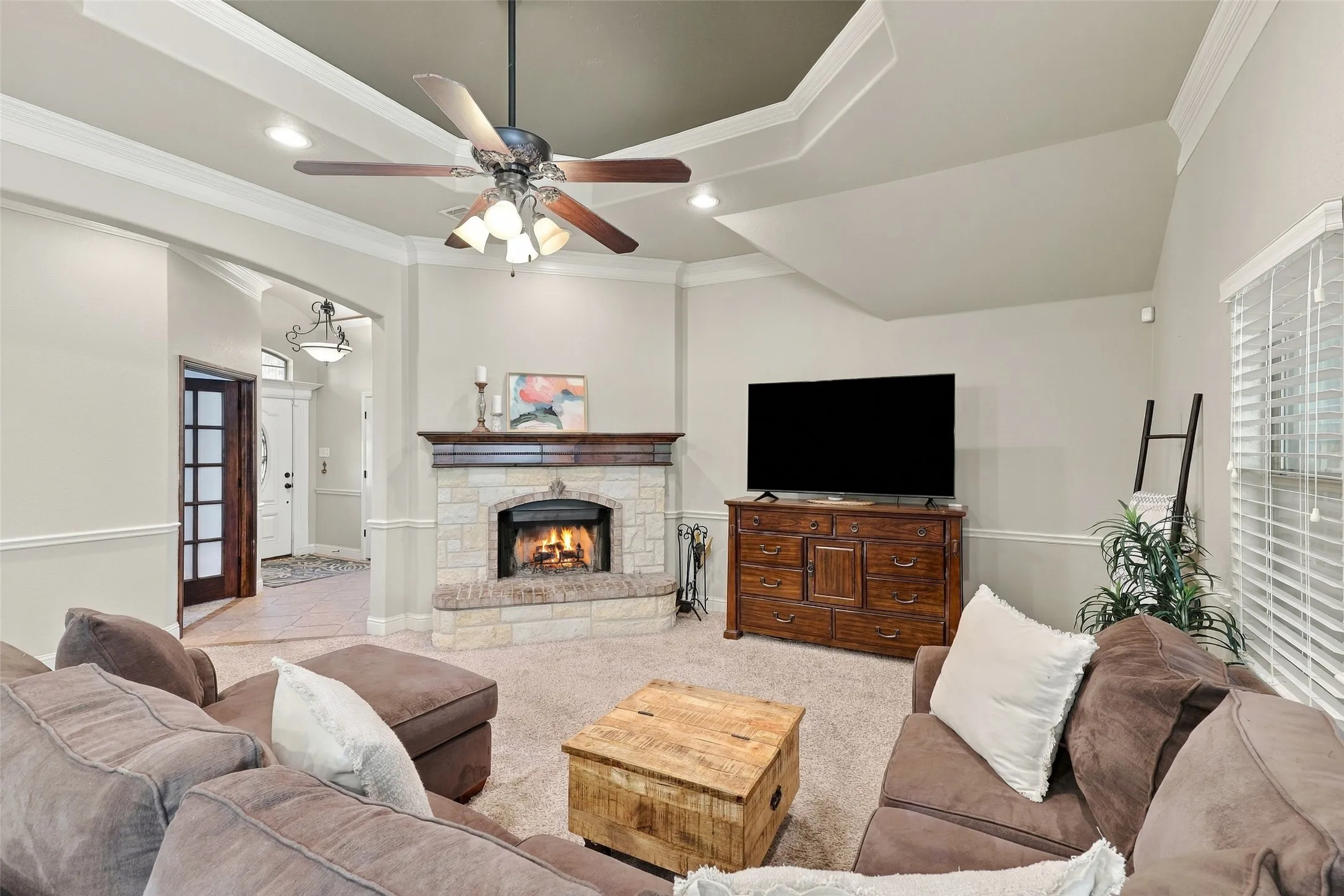 Living Room: Inviting living space features a floor-to-ceiling stone fireplace with wood mantel, elegant tray ceiling, crown molding, and abundant natural light.