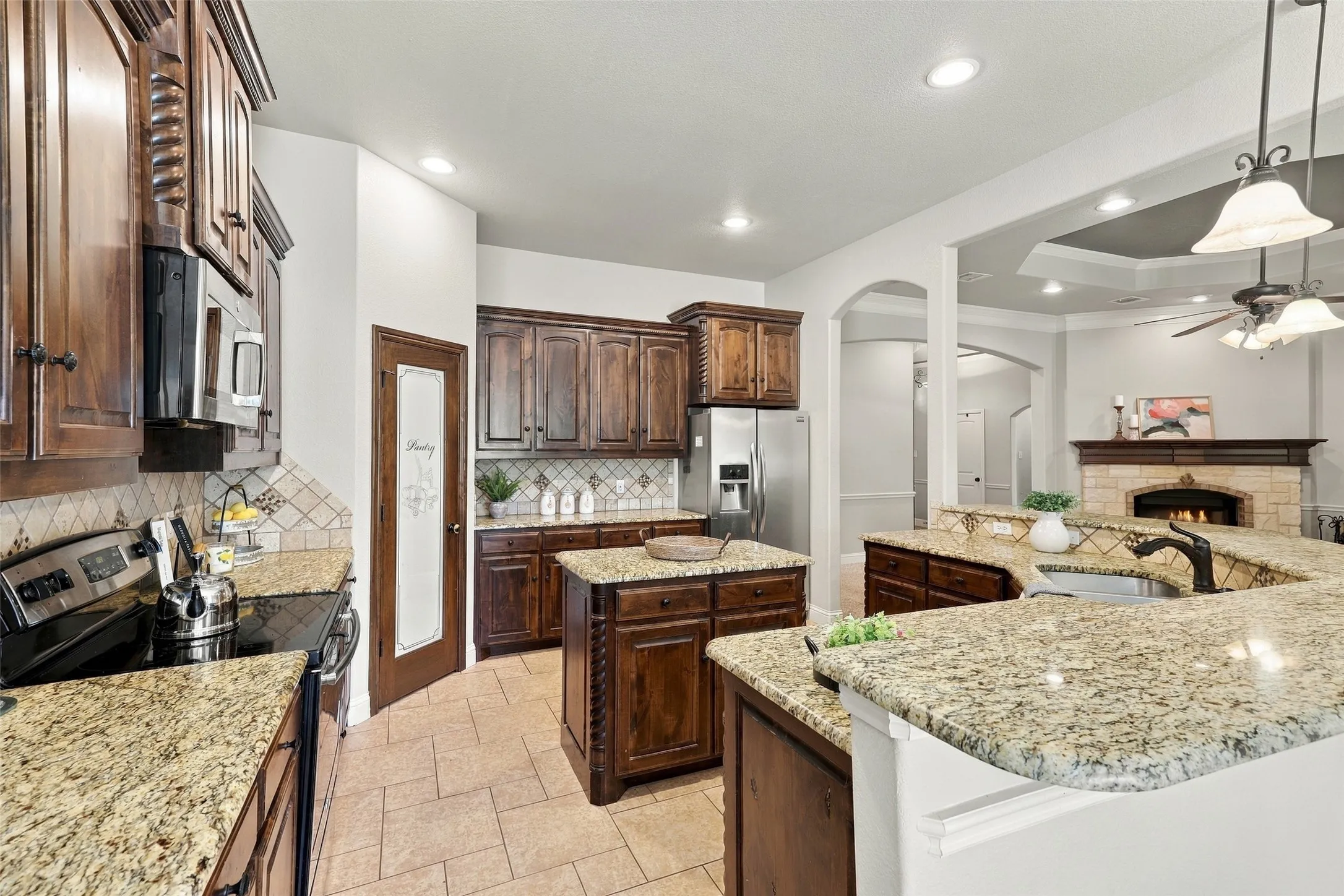 Kitchen: Spacious kitchen featuring rich wood cabinetry, granite countertops, a center island, and an open view into the living area with a stone fireplace.