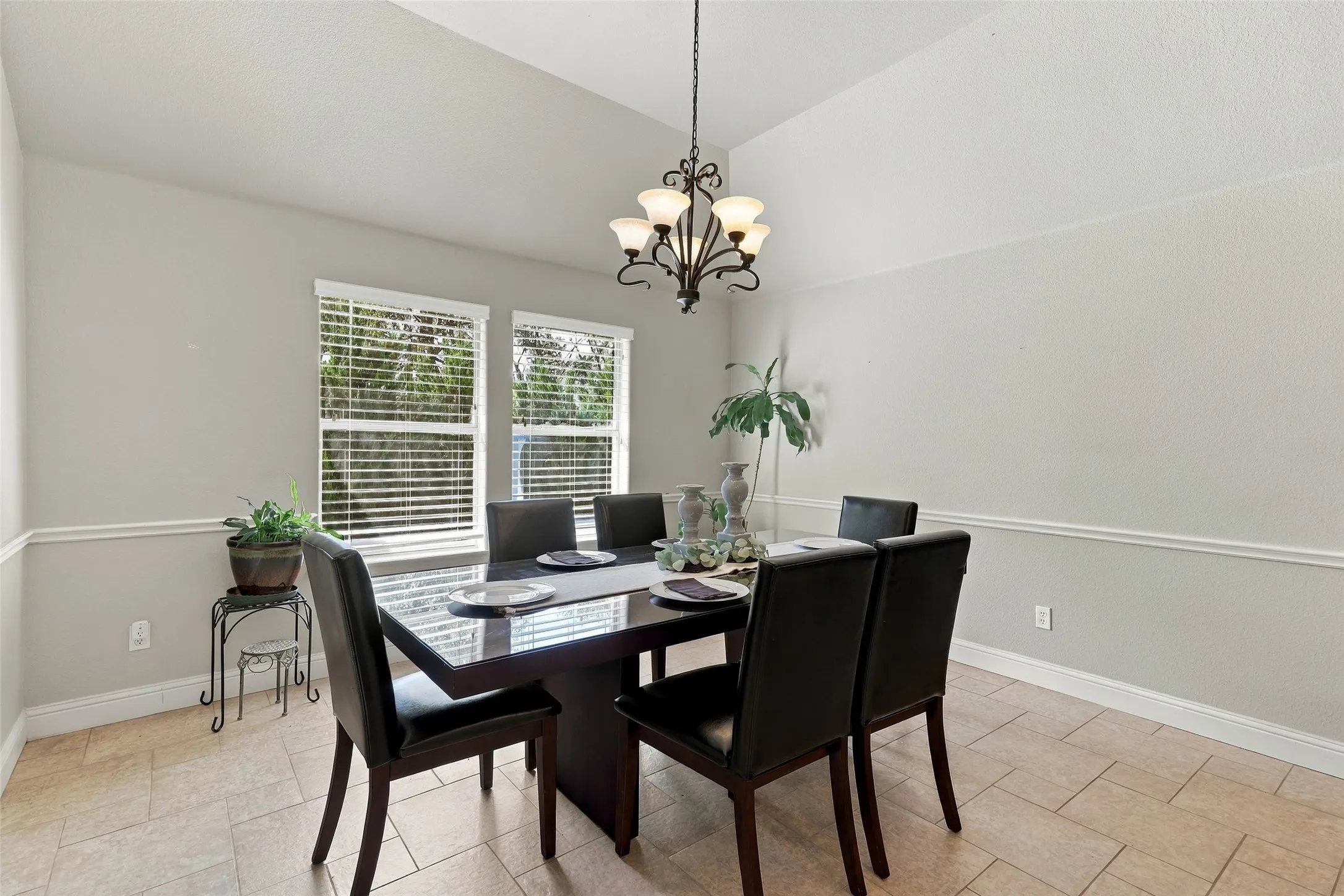 Dining Area: Bright dining space features vaulted ceilings, a decorative chandelier, tile flooring, and large windows overlooking the landscaped exterior.