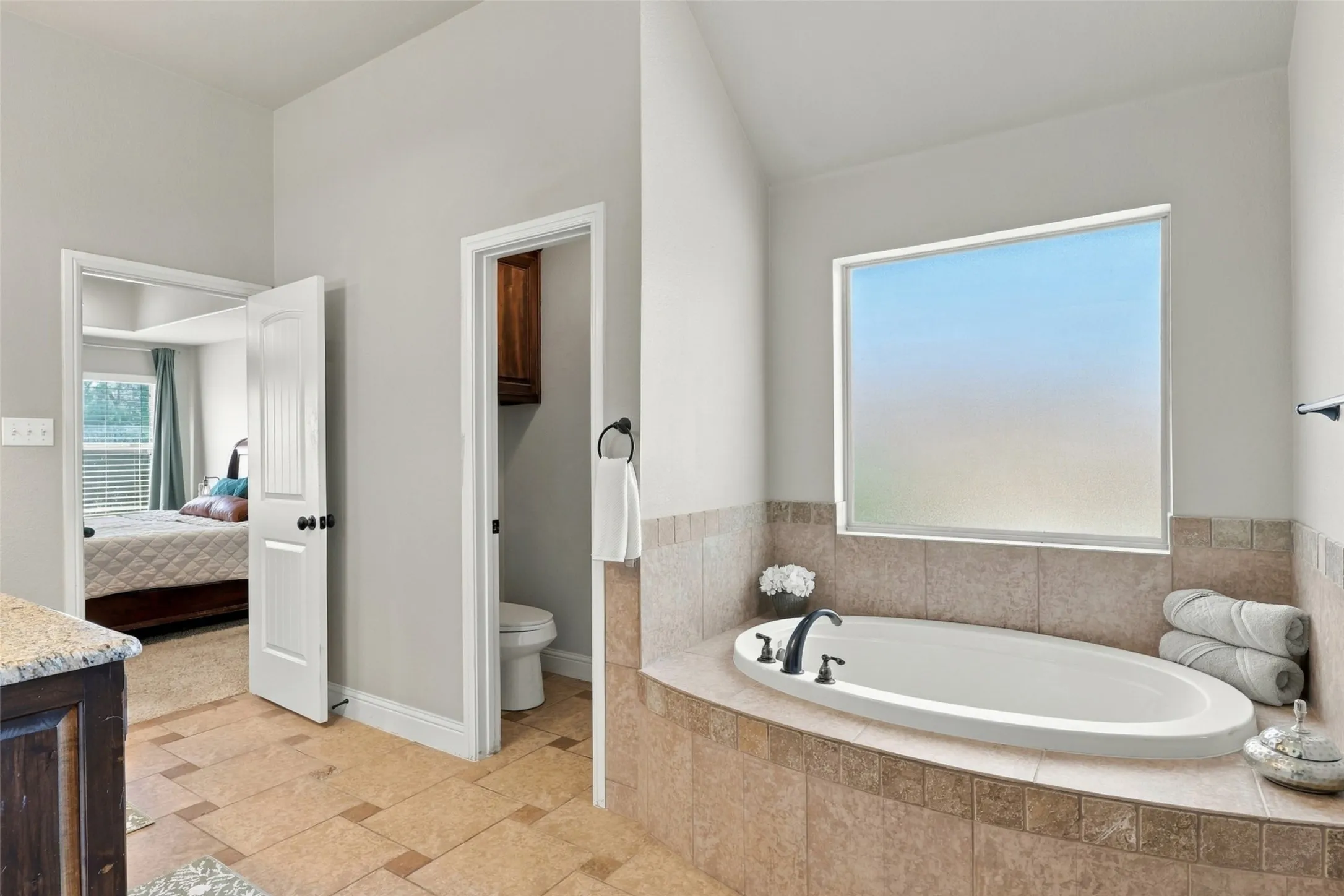 Primary Bathroom: Relaxing soaking tub with tile surround sits beneath a large frosted window, providing natural light and privacy.