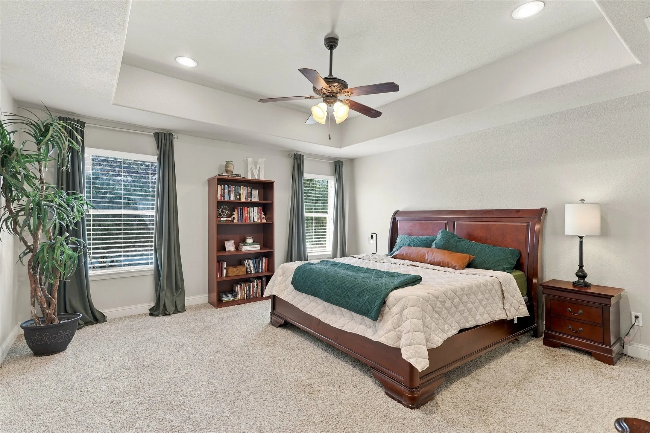 Primary Bedroom: Generously sized retreat features a tray ceiling, recessed lighting, plush carpeting, and large windows providing natural light.