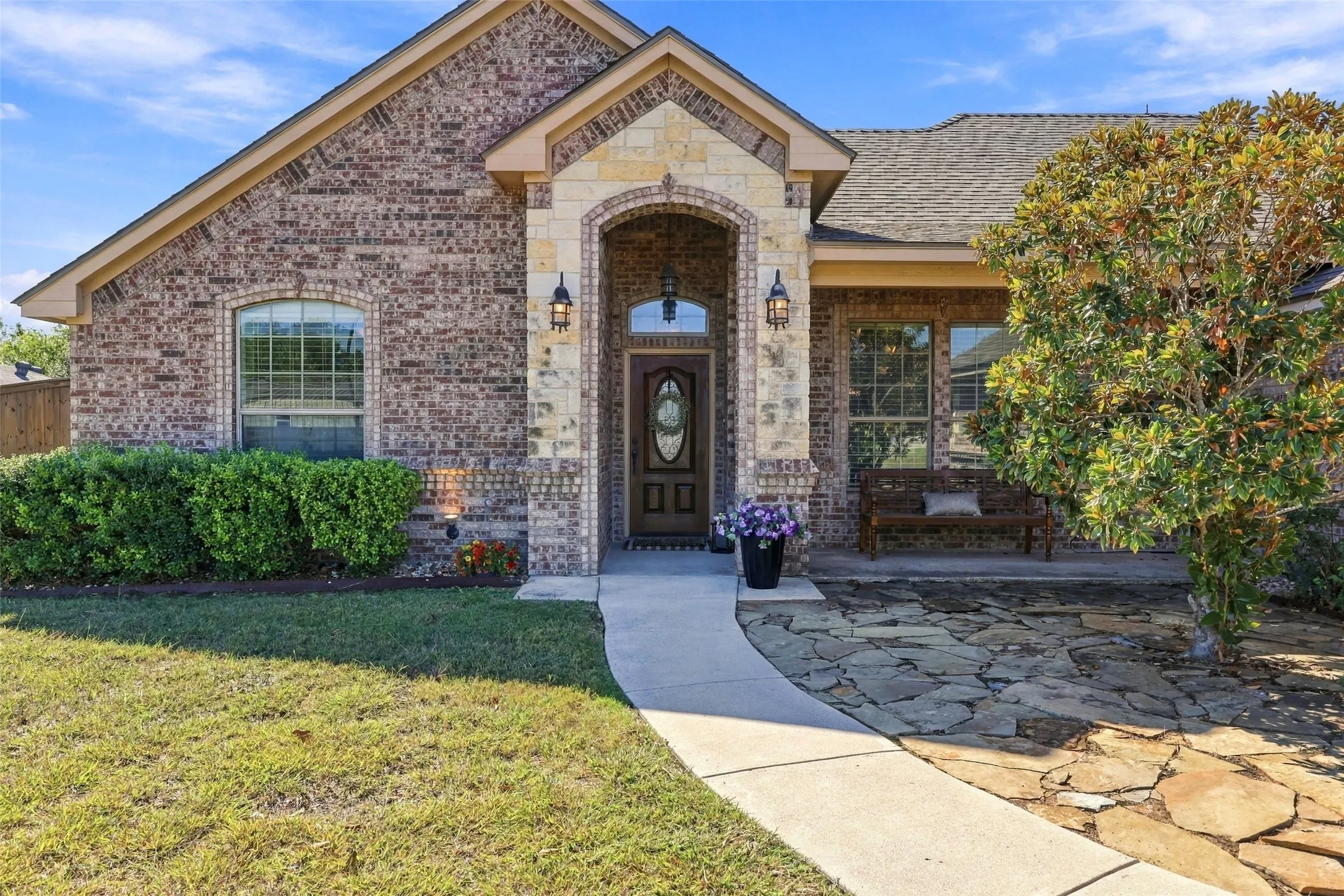 Front Entry: Covered entry showcases an arched stone surround, decorative glass front door, flagstone courtyard, and established landscaping.