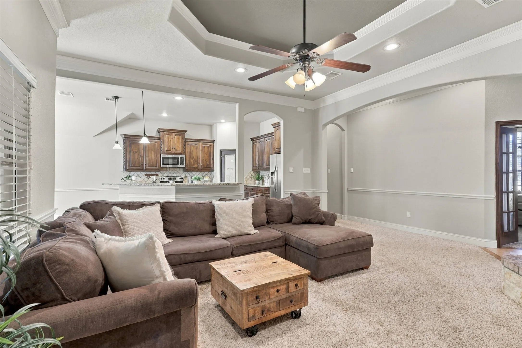 Living Room: Spacious open-concept living area showcases a decorative tray ceiling, recessed lighting, and seamless flow into the kitchen.